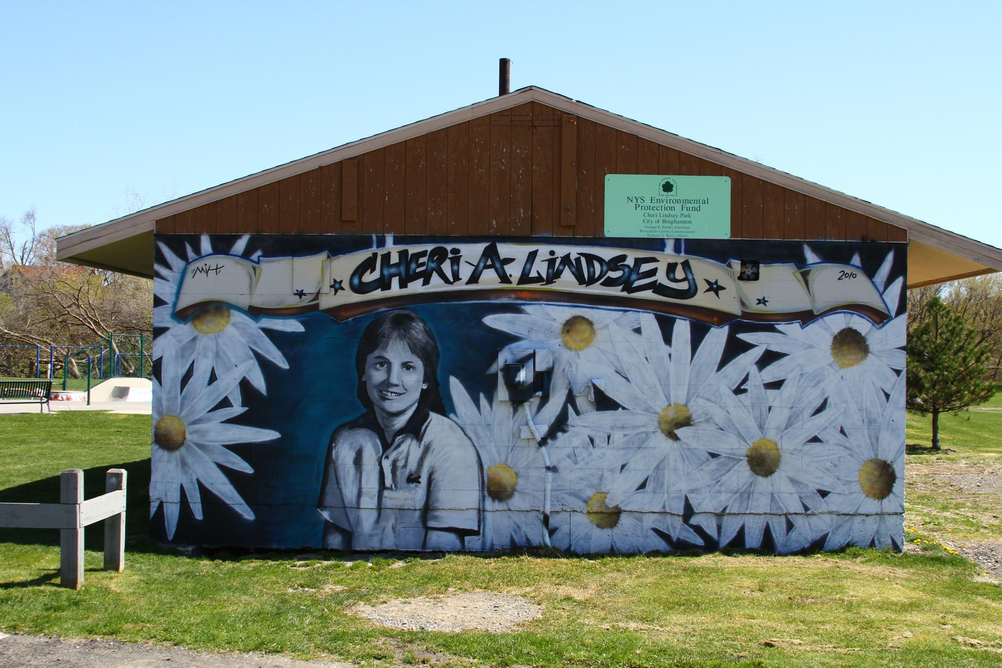 Bright mural of a person and daisies on a building in a sunny park.