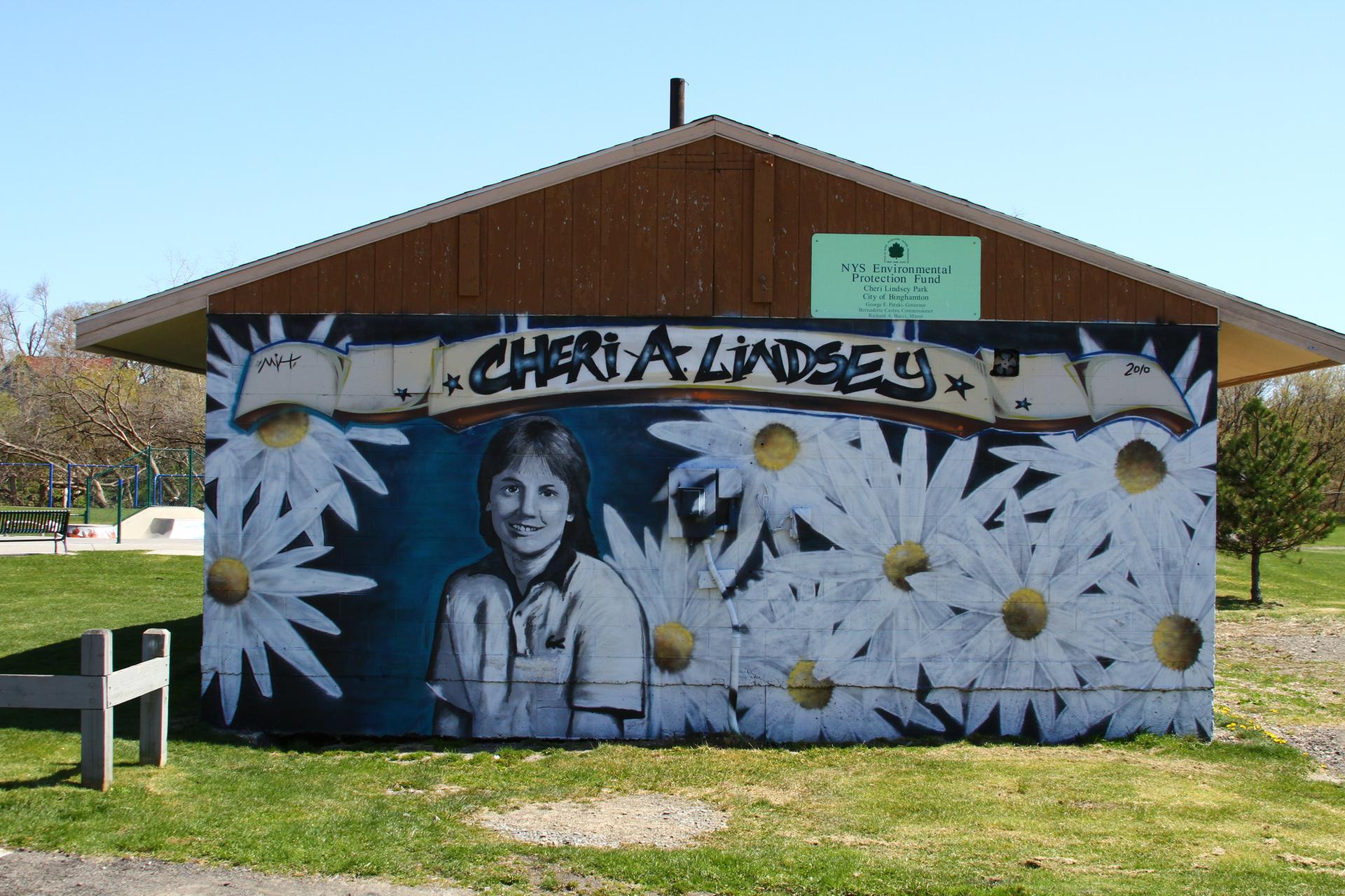Bright mural of a person and daisies on a building in a sunny park.