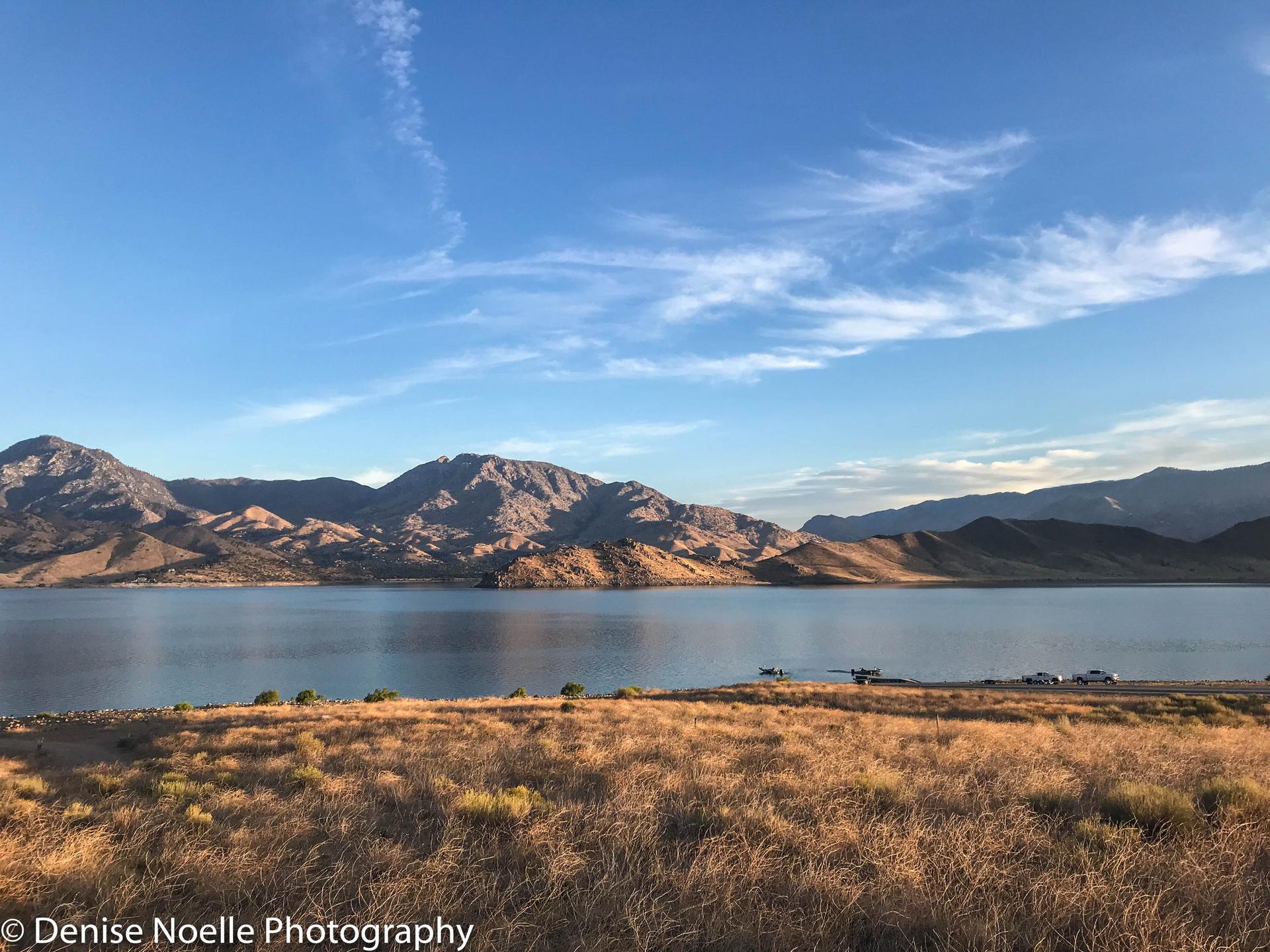 A vast lake with rugged mountains and dry grass under a blue sky.