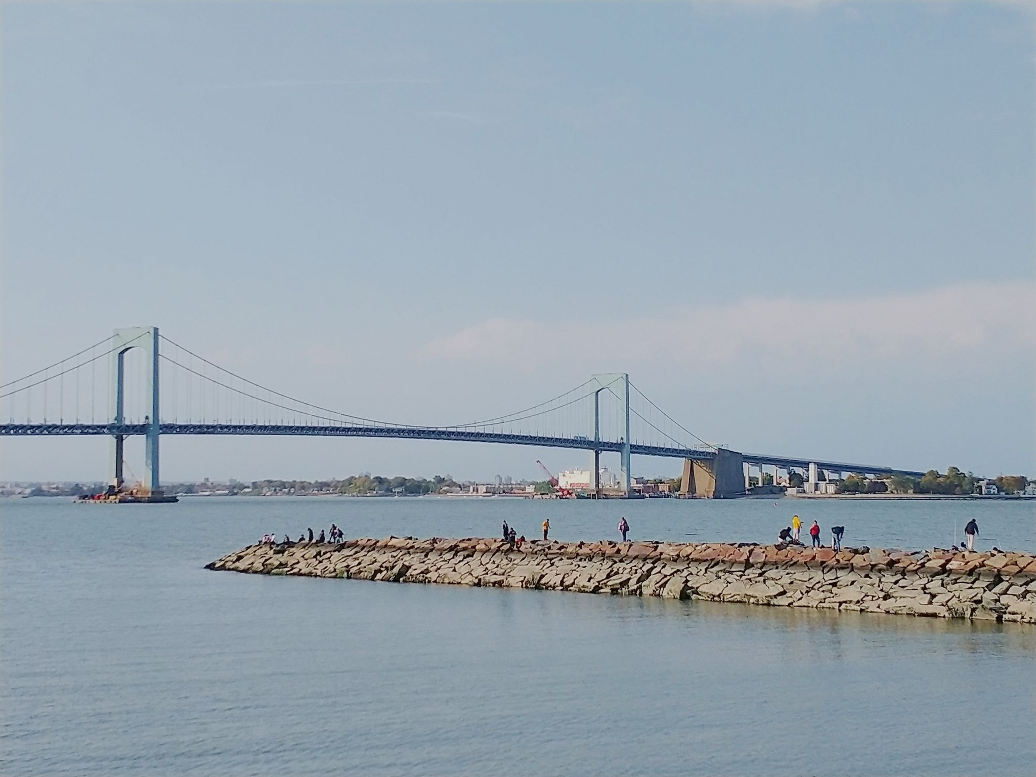 Numerous people on a rocky jetty with a large suspension bridge in the distance. - Little Bay and Fort Totten Loop
