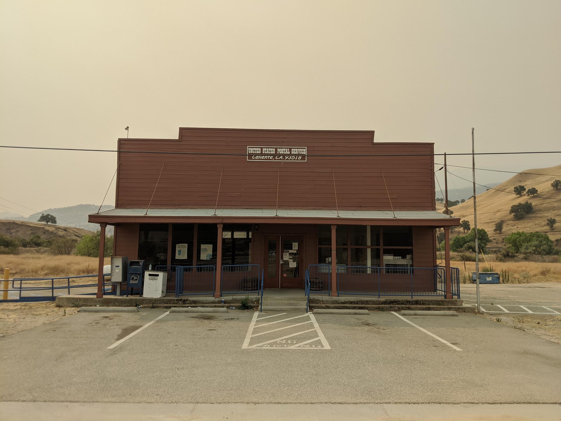 A brown building with a porch and parking lot under a hazy sky.