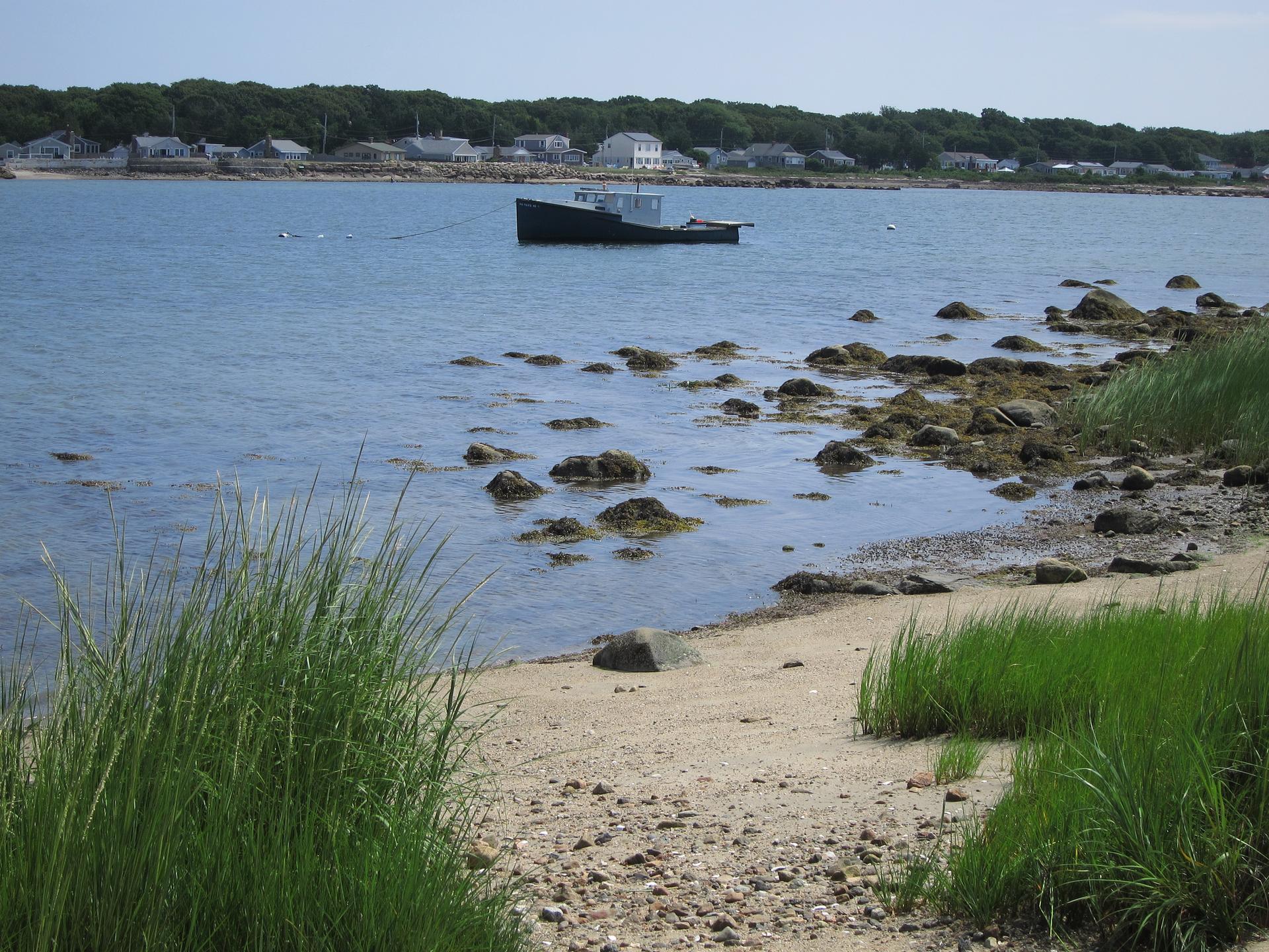 A small boat floats in a rocky bay with a distant town.