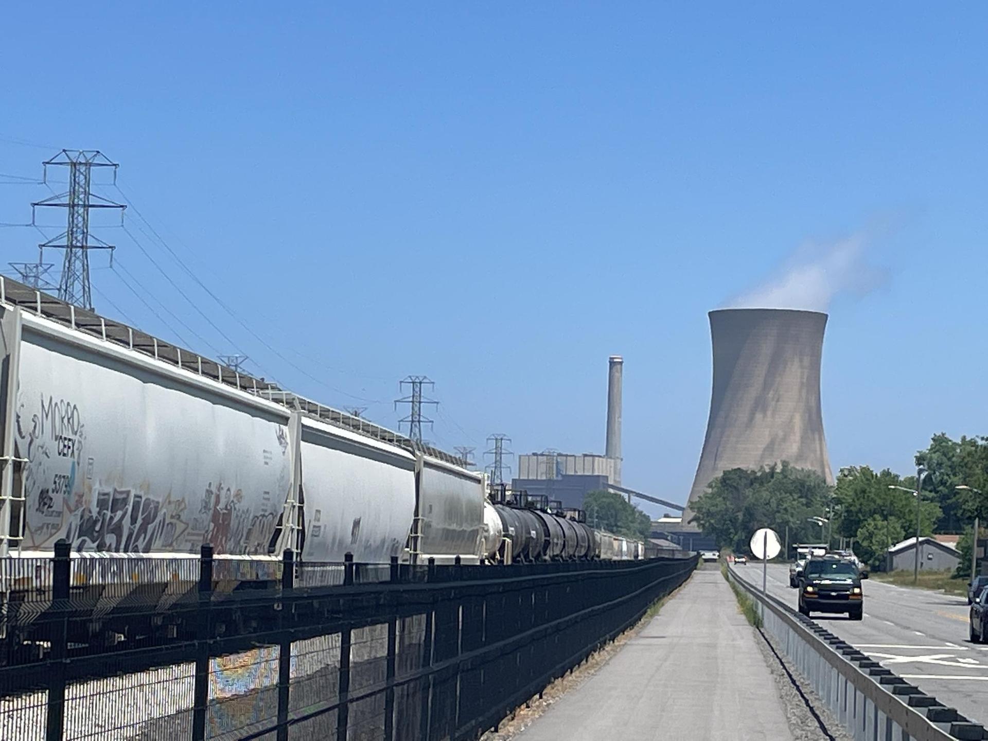 A long train passes a large cooling tower under a clear blue sky.