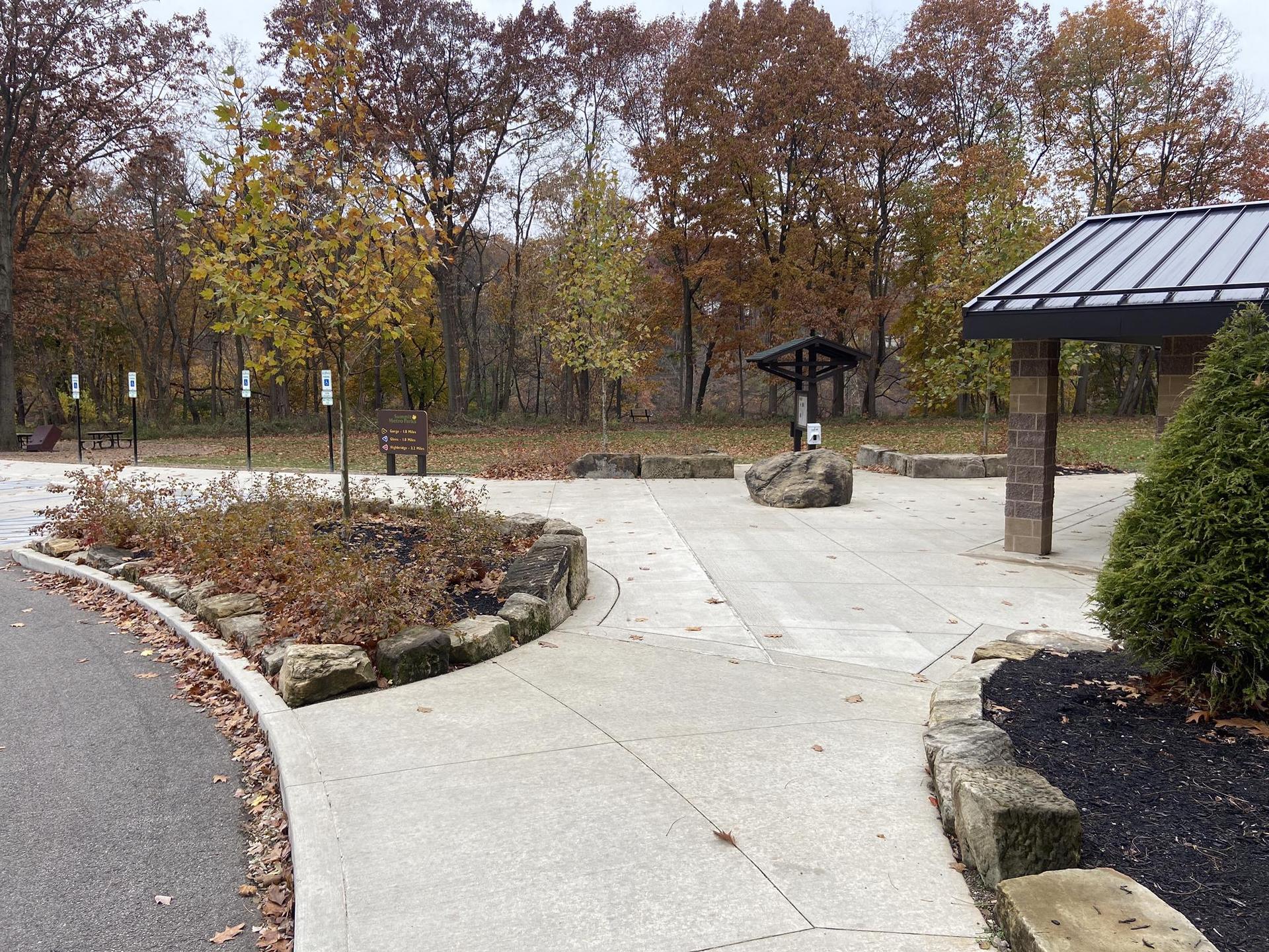 Paved area with autumn trees, a shelter, and landscaping under an overcast sky.