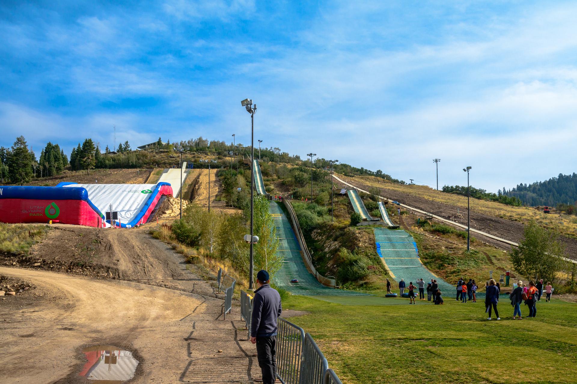Sunny view of people near ski jumps and an inflatable structure on a hill.