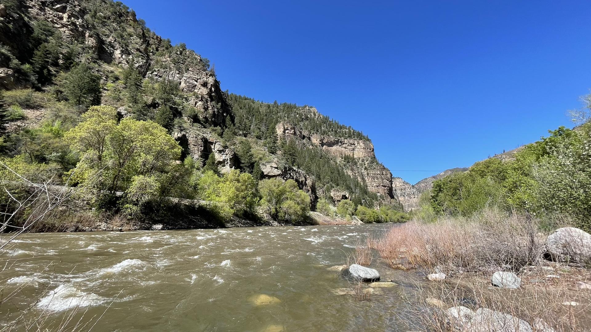 Rushing river in a deep canyon, flanked by steep, rocky, forested cliffs.