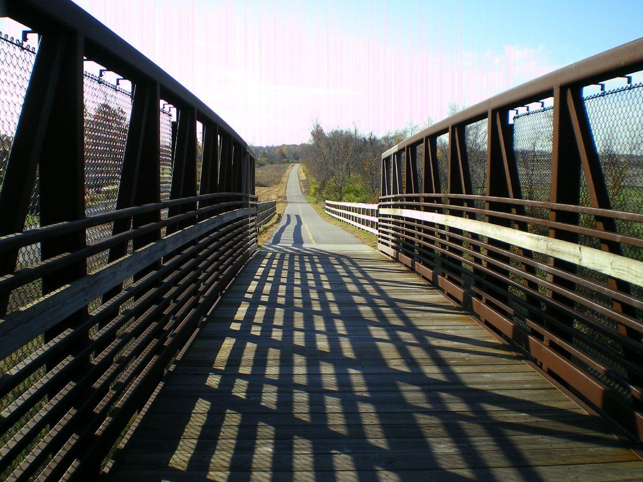 Sunny view from a wooden bridge with strong shadows onto a paved road.