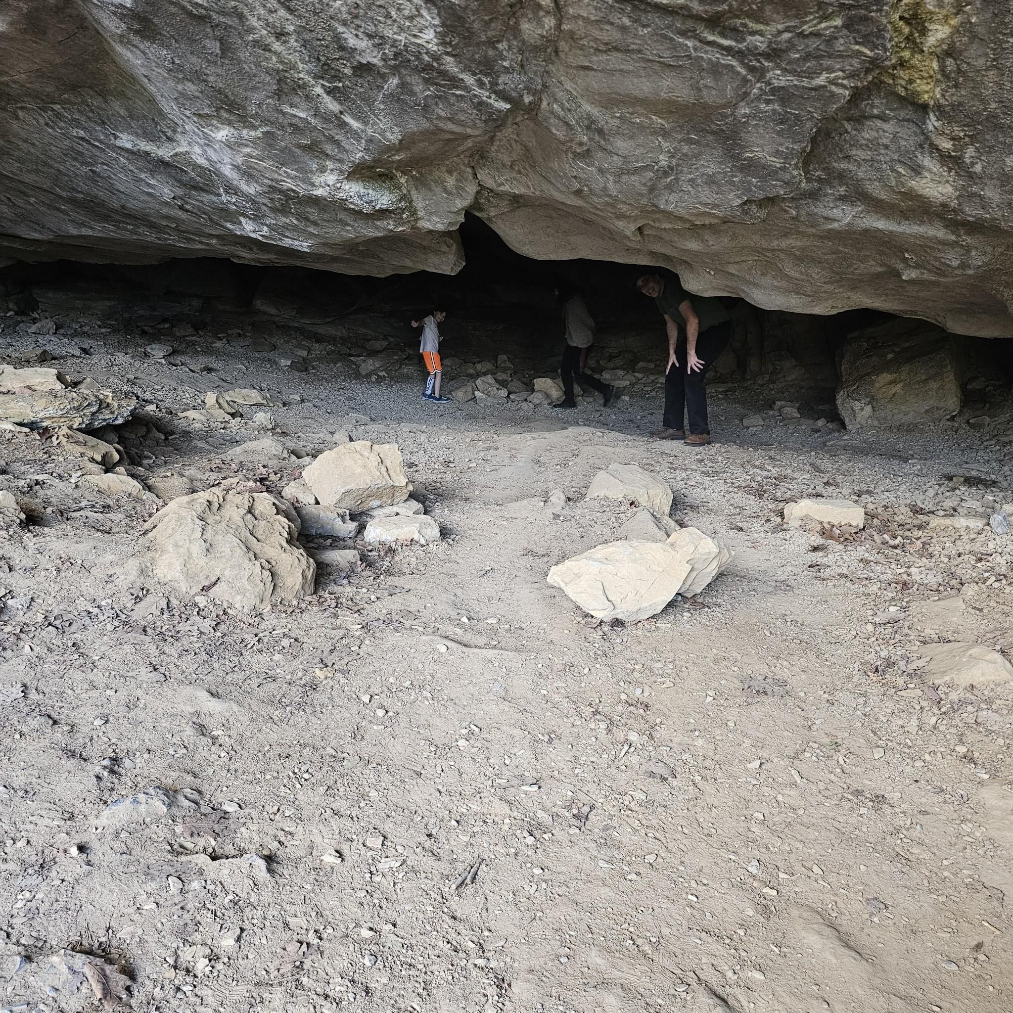 Three people exploring a dark, rocky cave interior. - Cedar Creek Trail