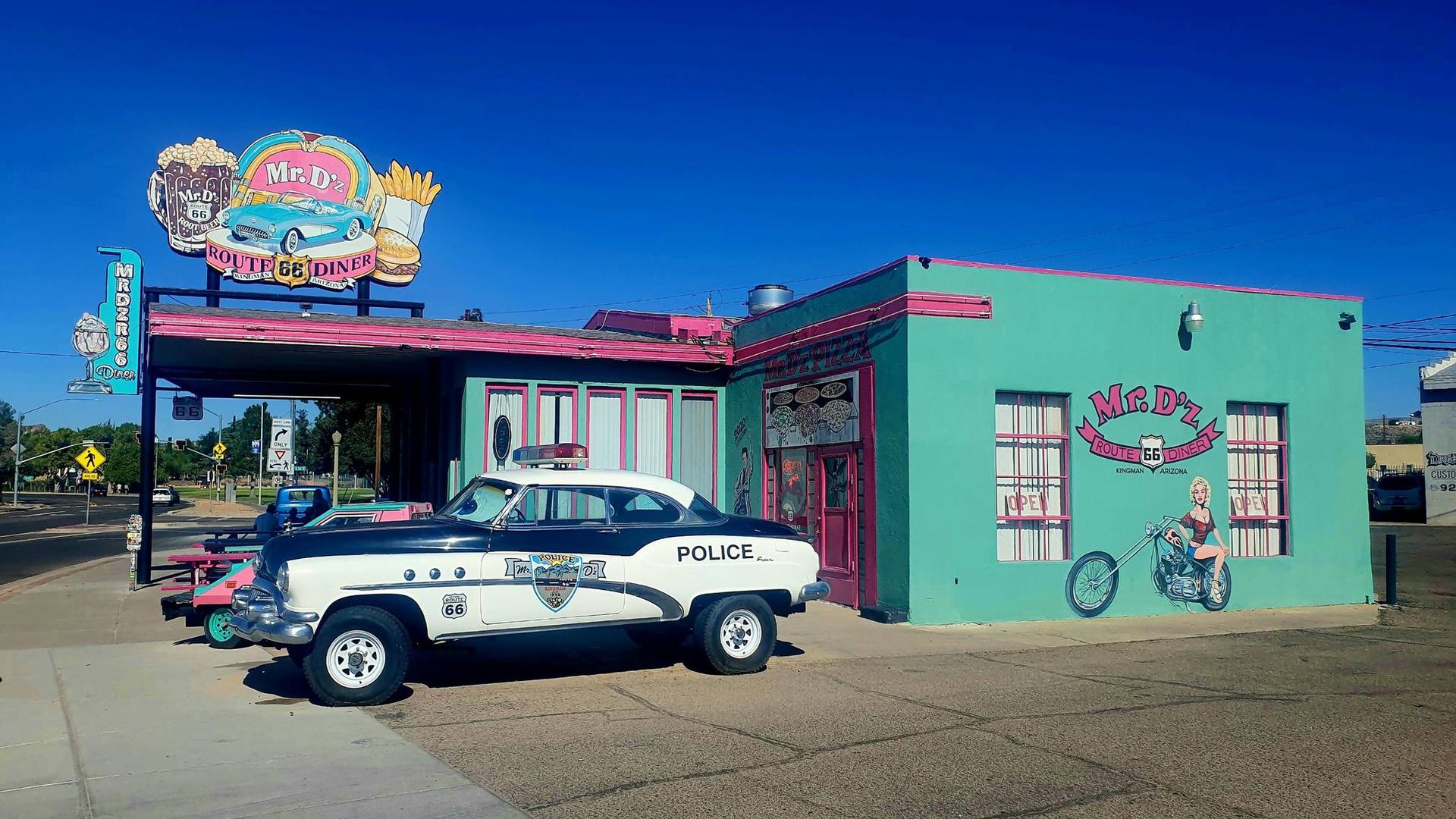 Vintage police car parked outside a colorful diner on a sunny day.