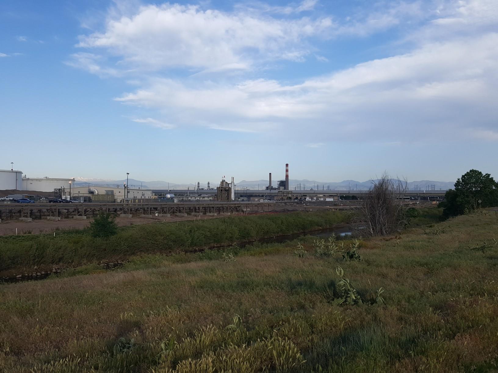 Distant industrial complex beyond a grassy field under a cloudy sky.