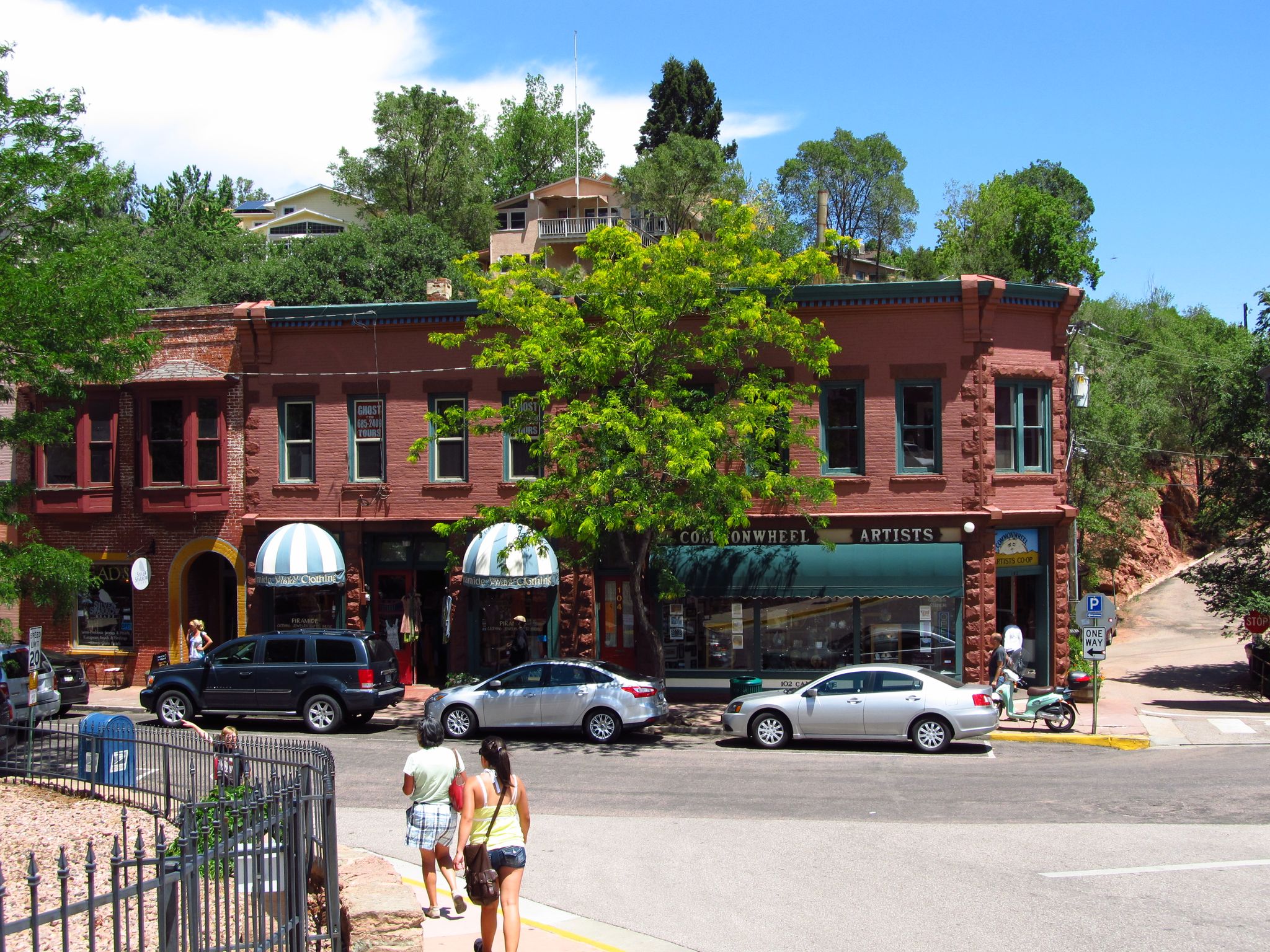 Brick buildings line a sunny street with cars and people walking on the sidewalk. - Memorial Park, Manitou Springs – Manitou Avenue loop from Garden of the Gods
