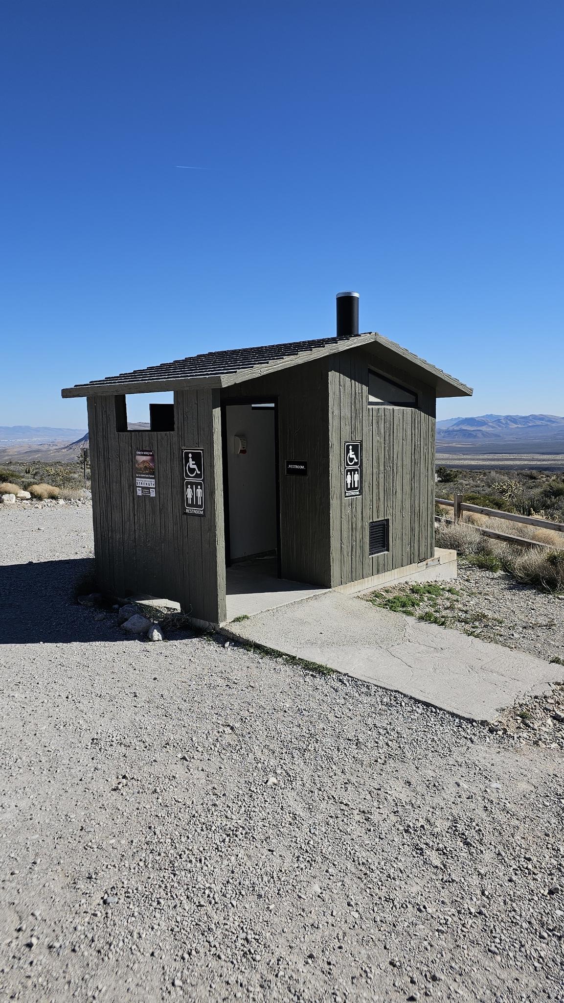 A small, gray wooden outhouse building under a clear blue sky.