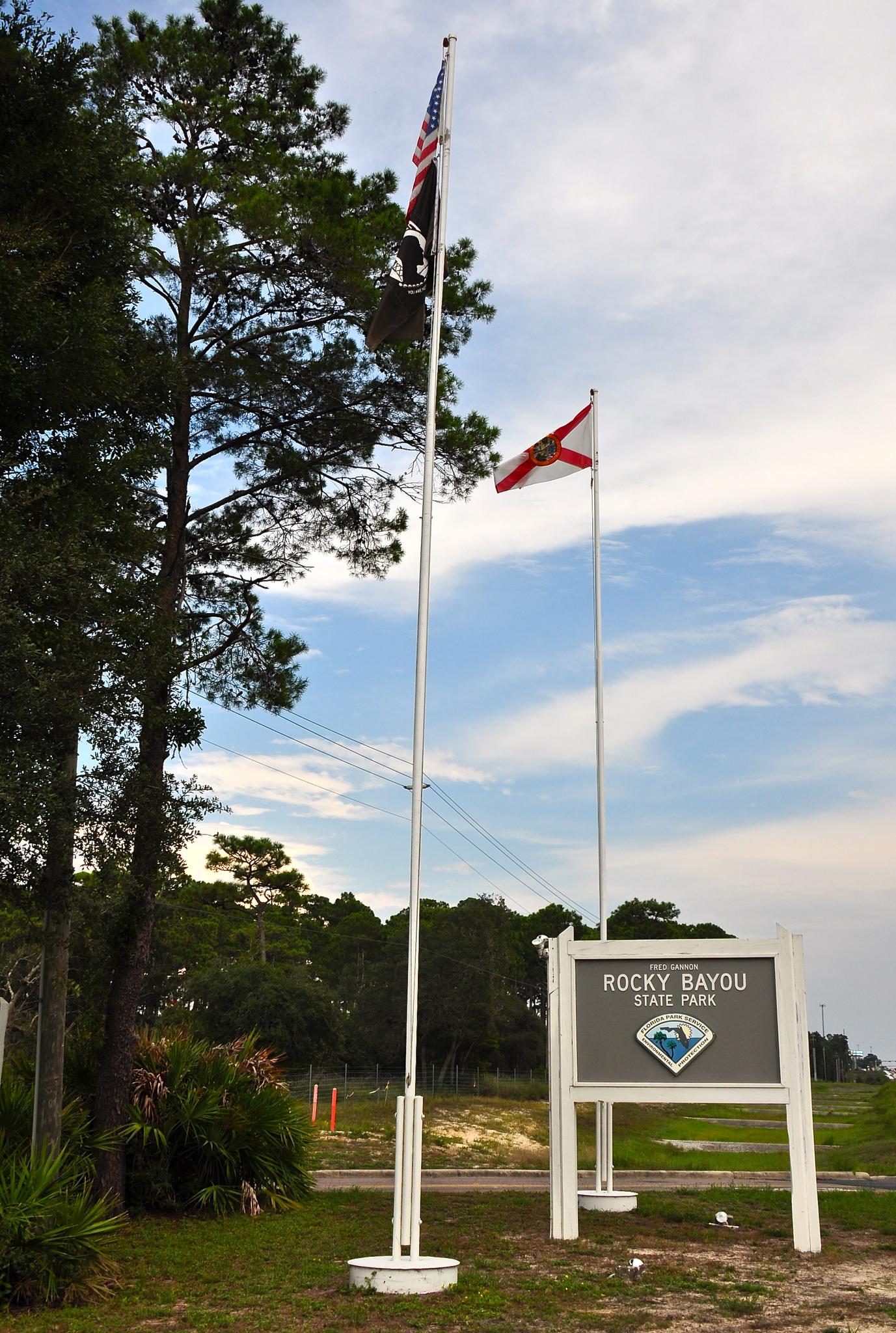 Two flagpoles with flags stand beside a sign under a cloudy sky.