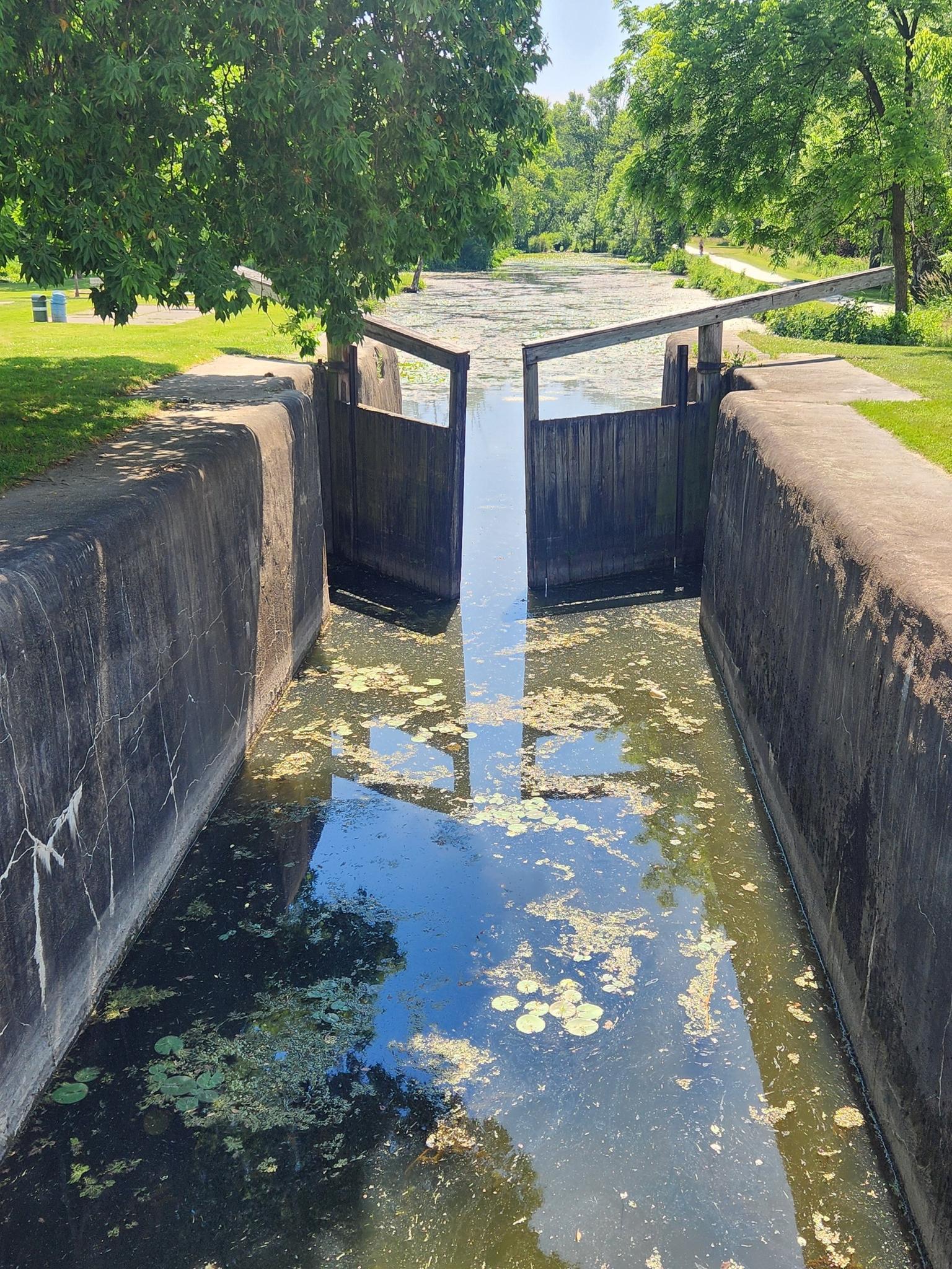 A canal lock with open gates, reflecting sunlight on the water.