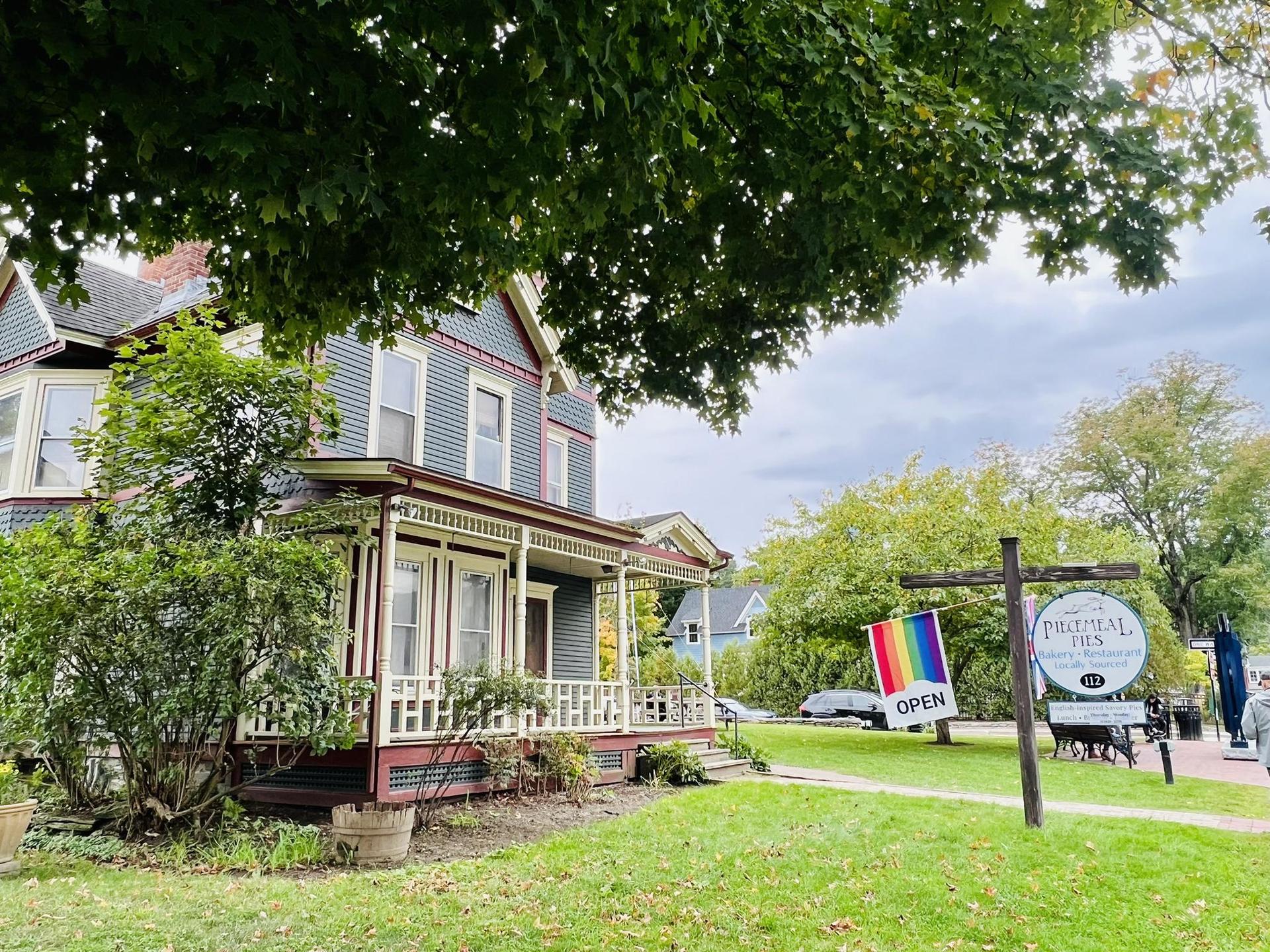 Ornate house with a porch and "Open" sign under a cloudy sky.
