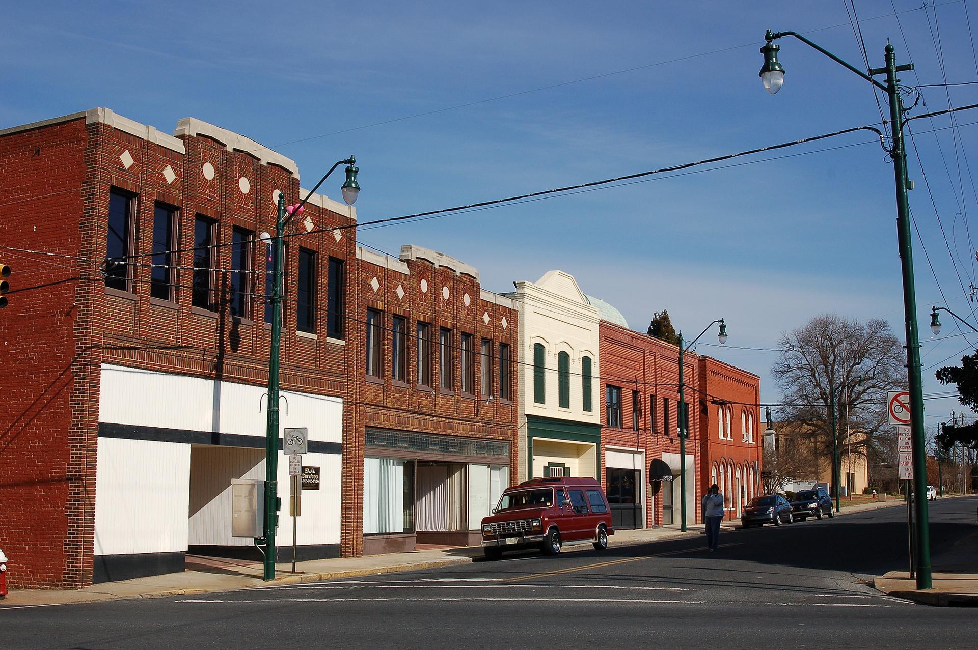Sunny street with historic brick buildings, parked cars, and a person walking.
