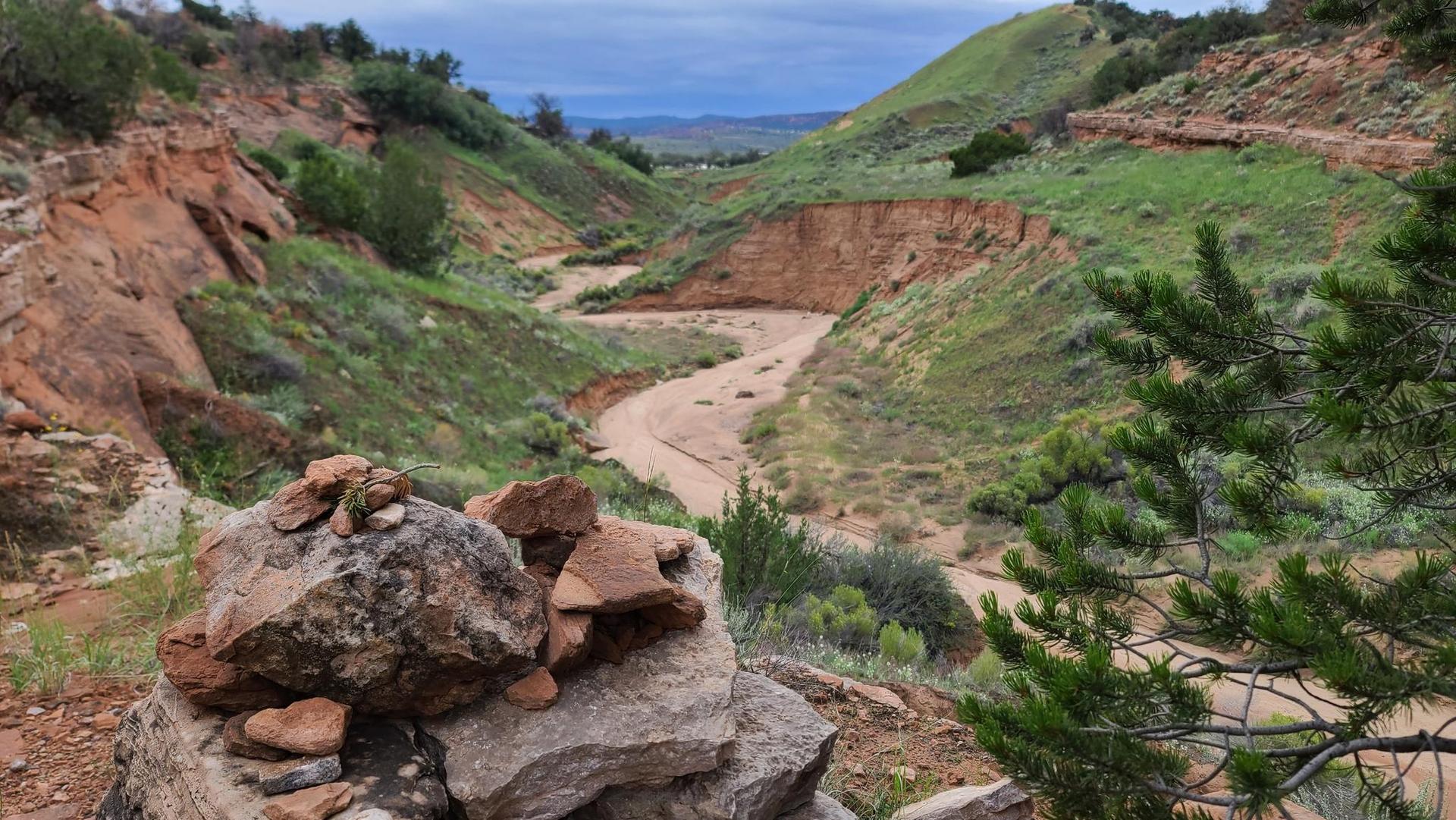 Overcast view of a winding dry riverbed through green and red hills.