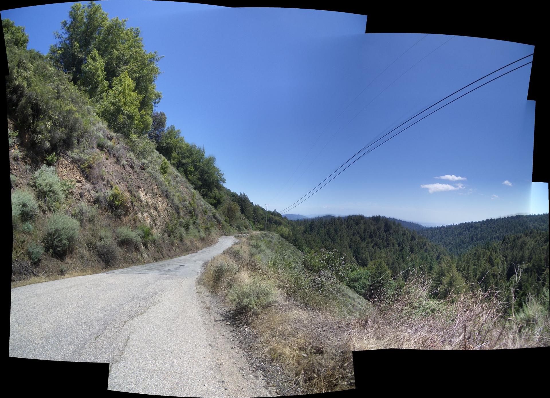 Winding paved road alongside a steep, green hillside under a clear sky.