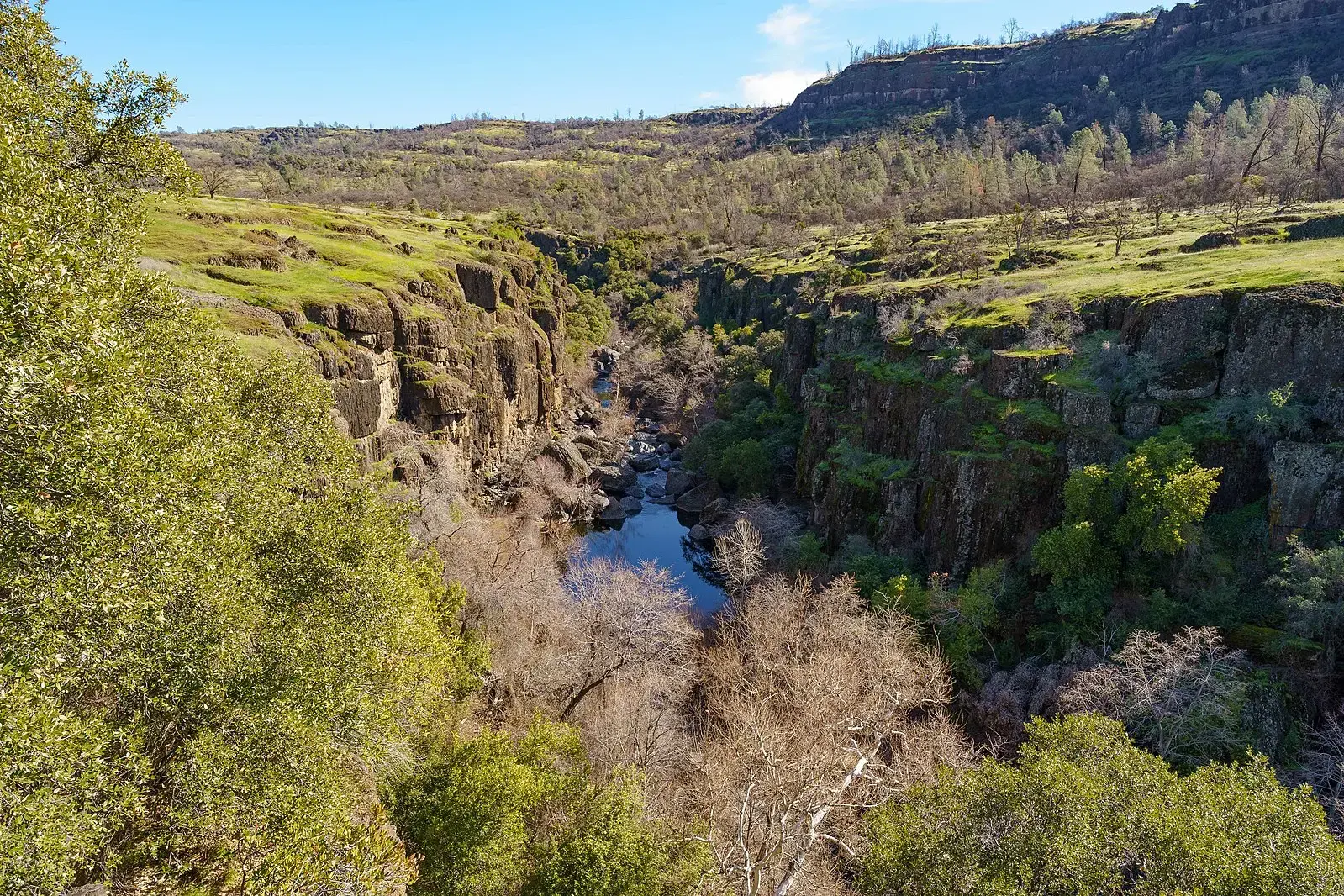 A river winds through a deep, rocky canyon under bright daylight.