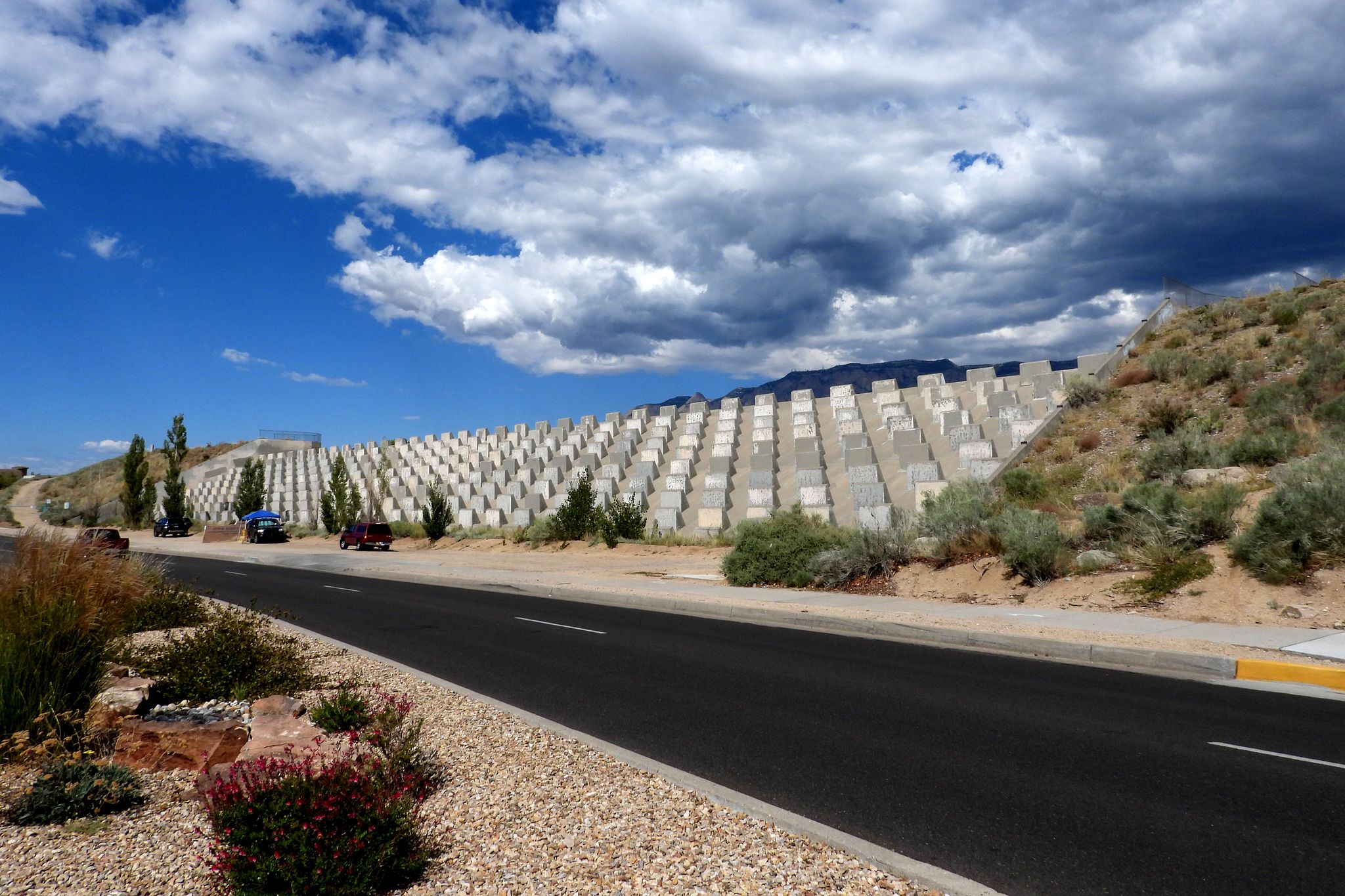 Road runs alongside a large, terraced hillside retaining wall under cloudy sky. - Bear Canyon Open Space Loop