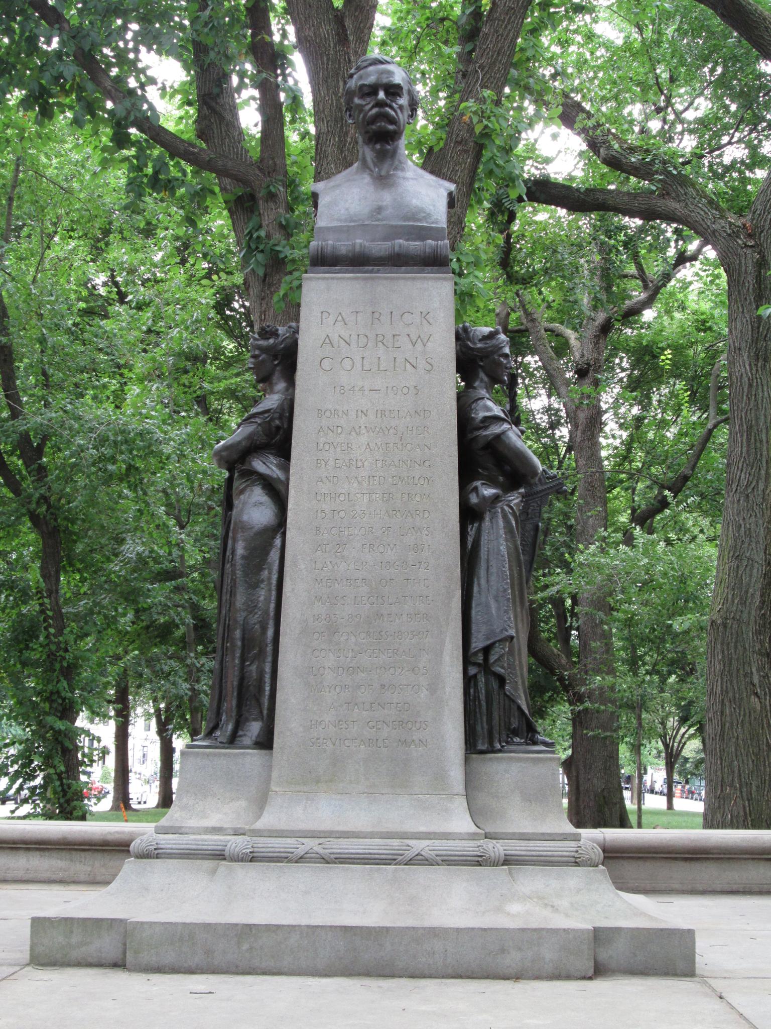 A tall stone and bronze monument surrounded by green trees.