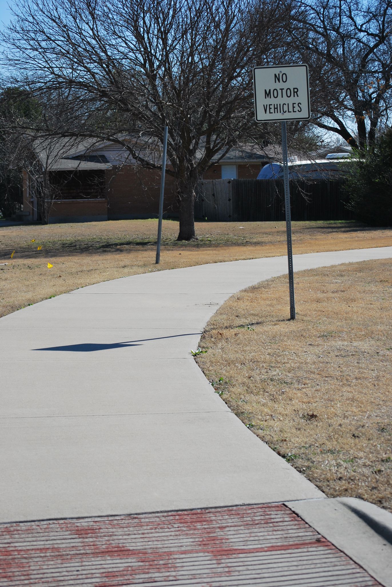 Paved path curving right with a "No Motor Vehicles" sign under bare trees. - North Lakes Park loop
