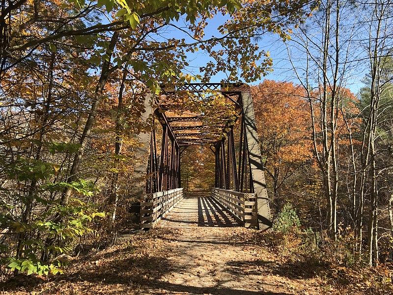 A metal truss bridge over a path, framed by vibrant autumn foliage.
