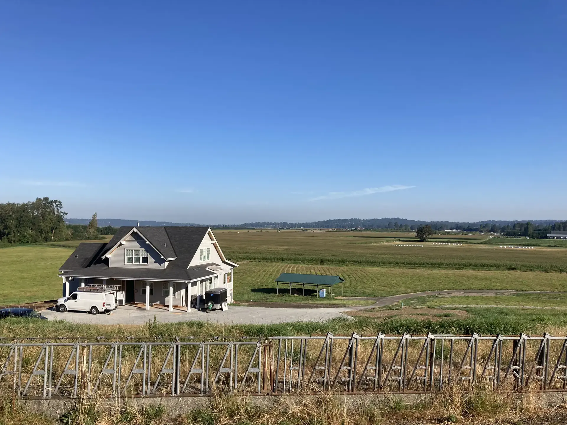 Sunny rural landscape with a large house, green fields, and a distant fence.