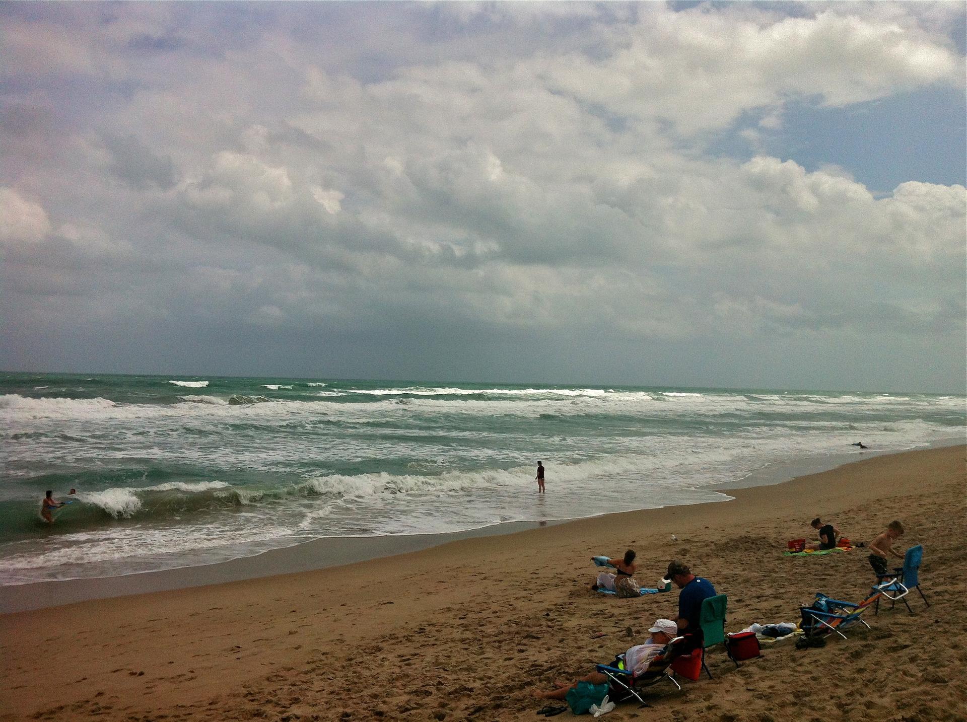 People relaxing on a sandy beach with waves crashing under a cloudy sky.