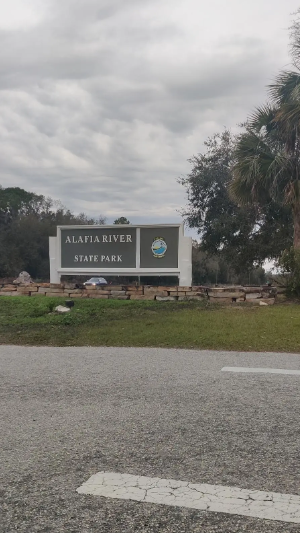 Large park entrance sign next to a road under a cloudy sky.