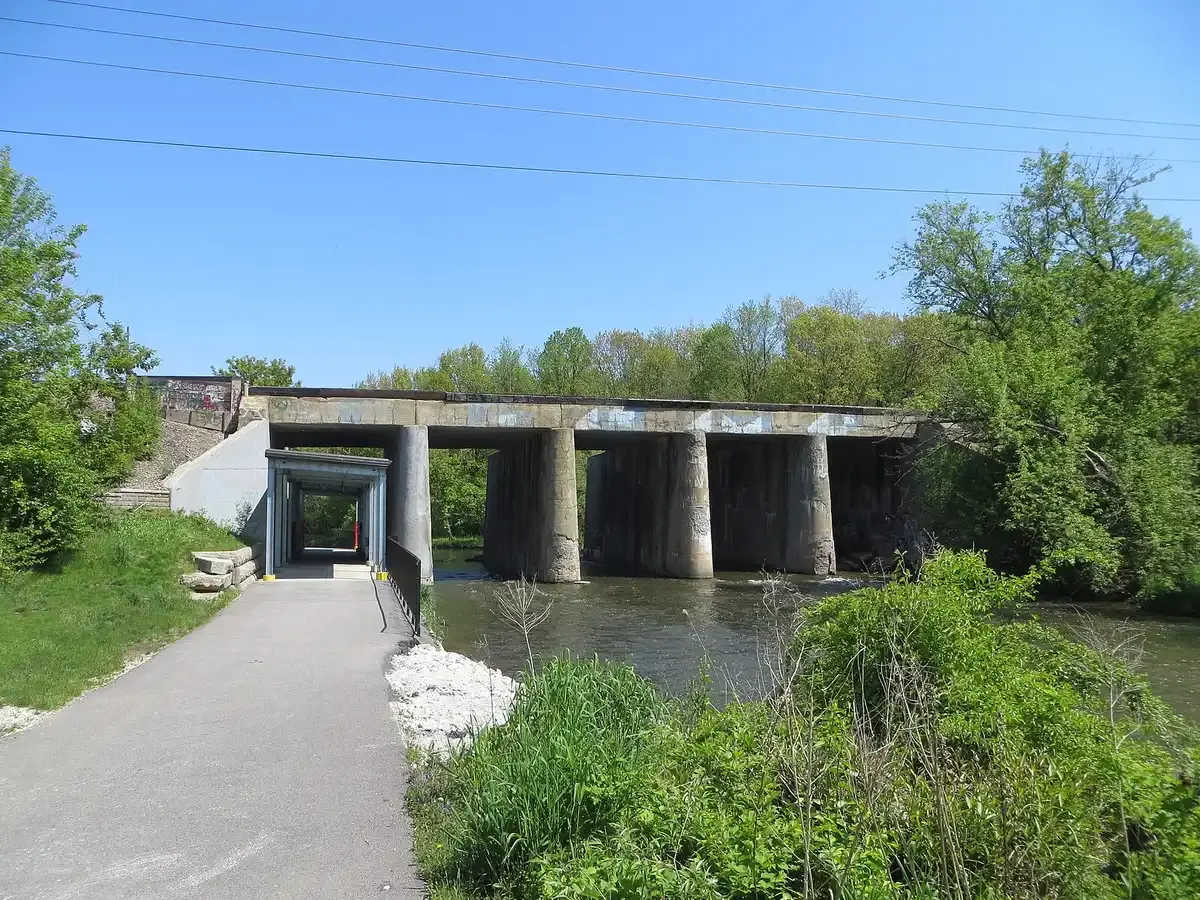 A concrete bridge spans a river, with a paved path and tunnel entrance nearby.
