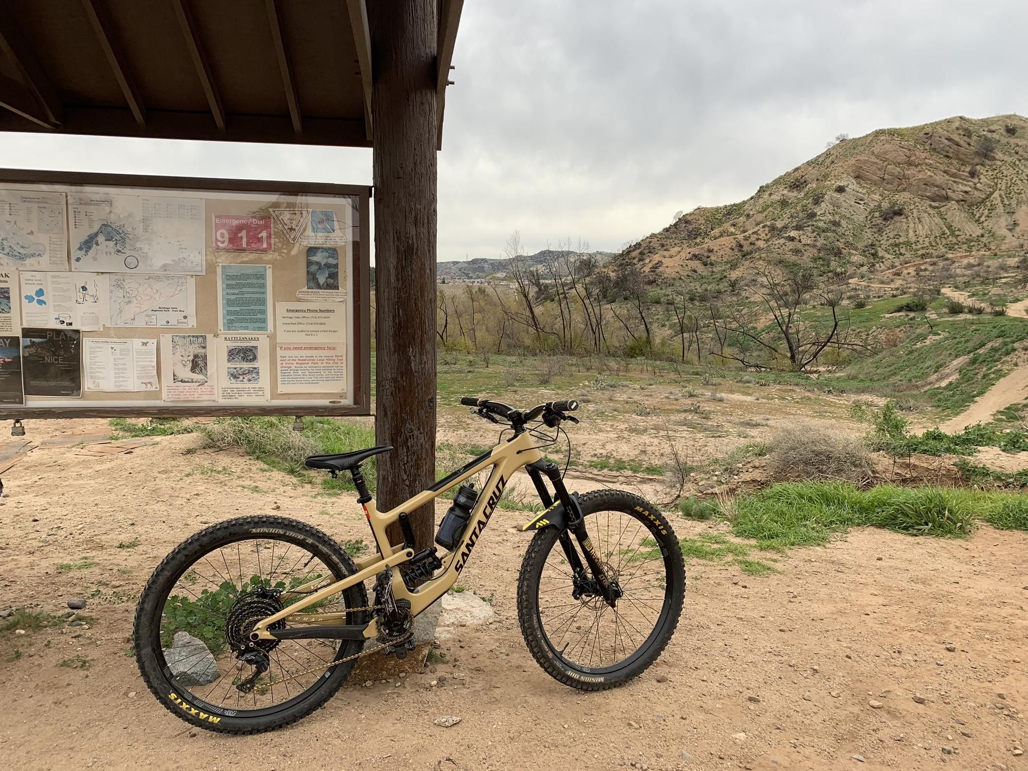 A mountain bike parked next to an outdoor information board on a cloudy day. - Roadrunner Loop Trail