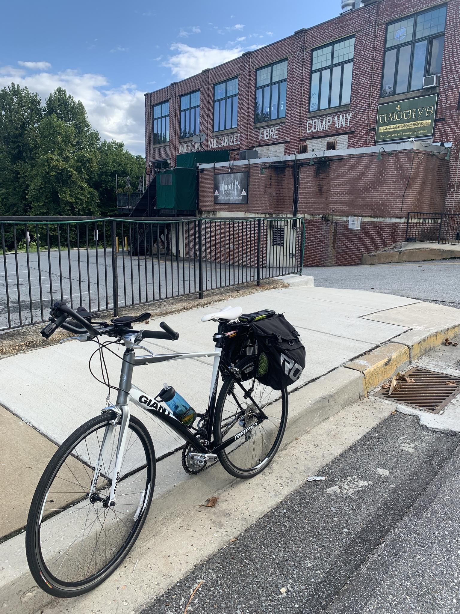 Bicycle with bags parked on a sidewalk next to a large brick building. - Fair Hill Trailhead – Olan Thomas Park loop from White Clay Creek State Park