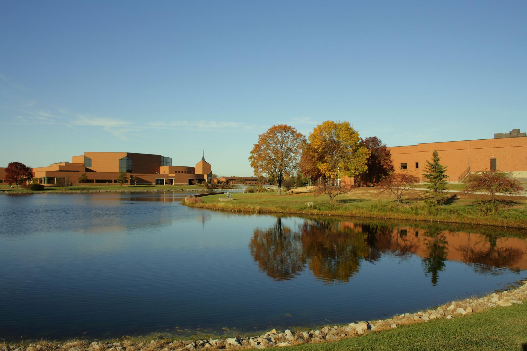 Calm lake reflects buildings and colorful autumn trees under a clear sky.