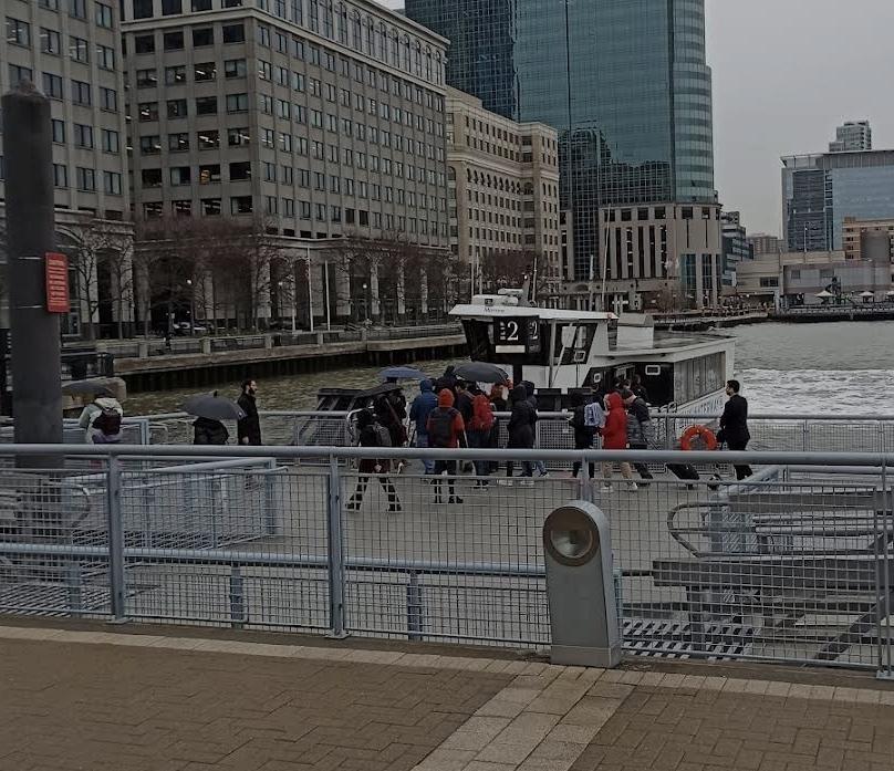 People waiting to board a ferry boat at a dock near tall buildings.