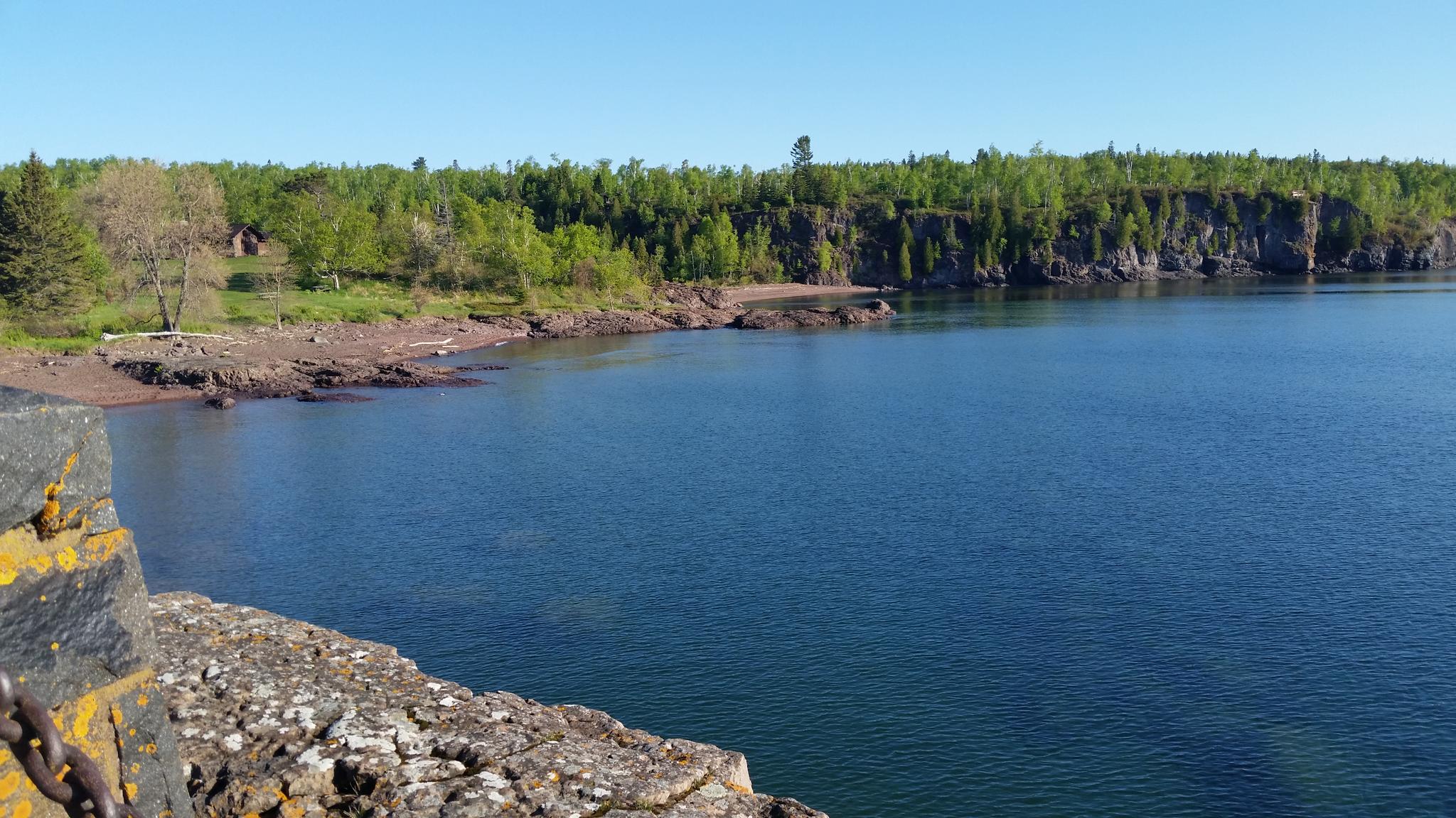 Sunny view of a blue lake, rocky cliffs, and green forest.