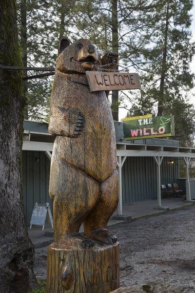 A tall wooden carved bear statue holding a 'Welcome' sign outdoors.