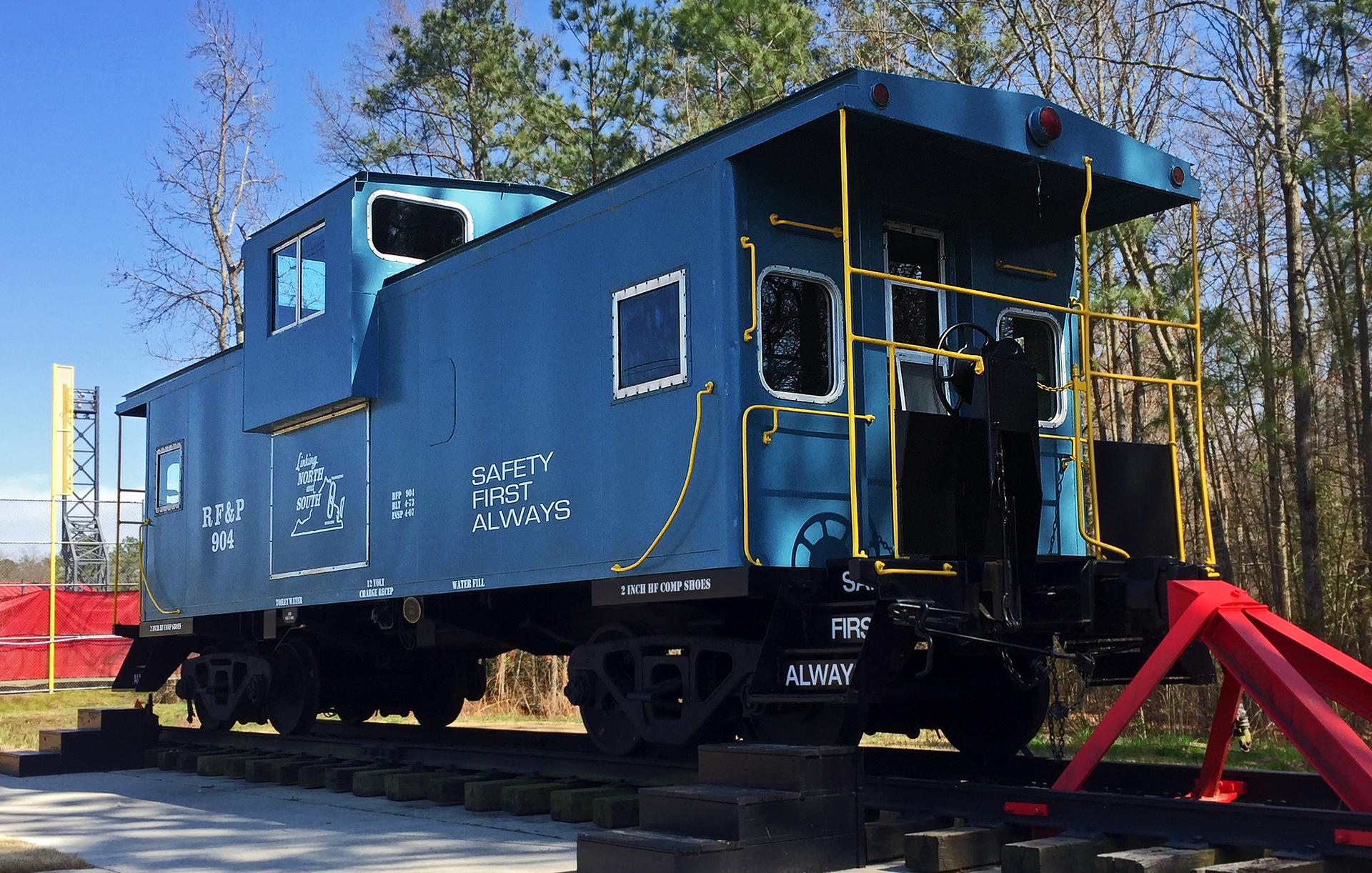 A bright blue train caboose on tracks, with trees in the background.