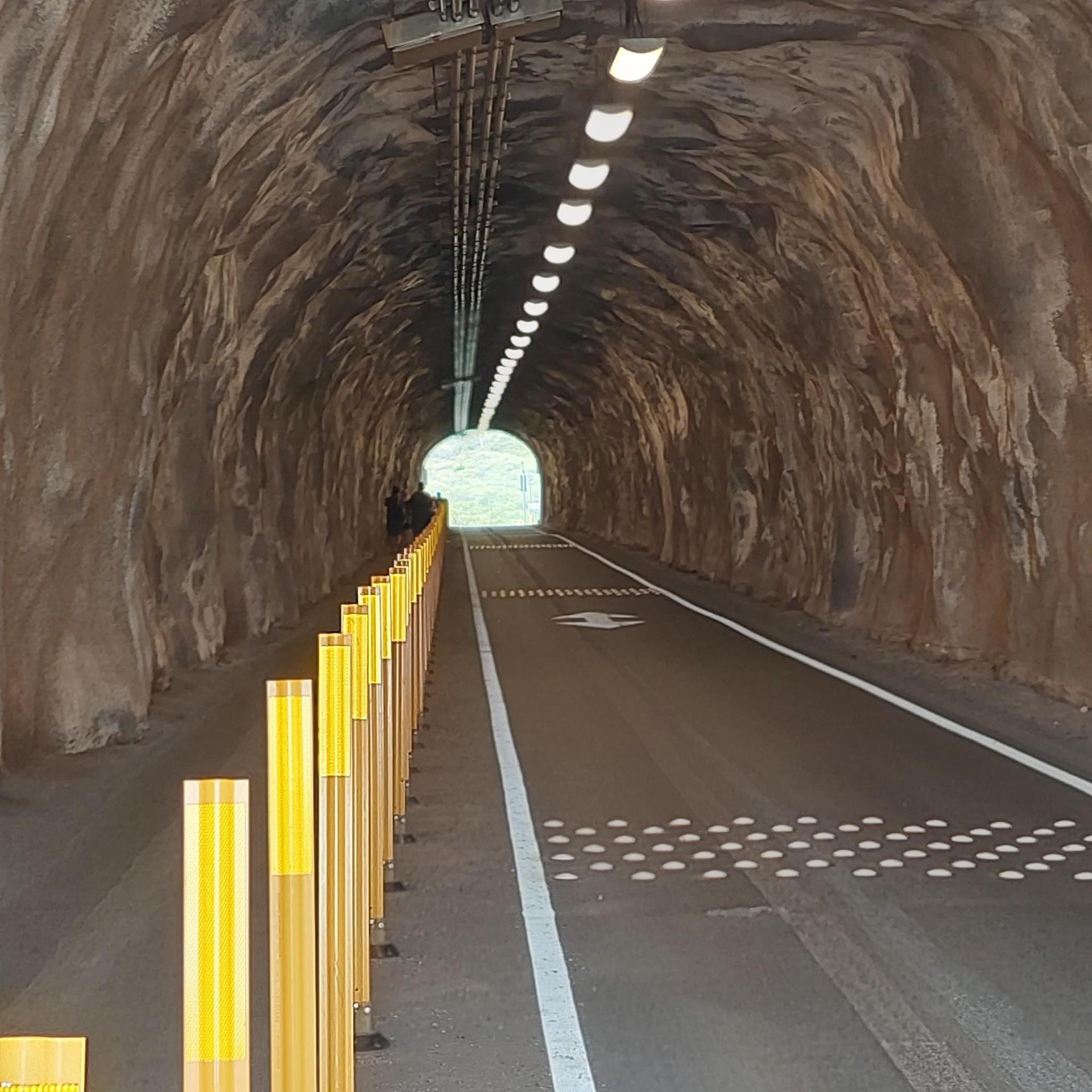 Lit tunnel with a paved path, yellow bollards, and light at the end.