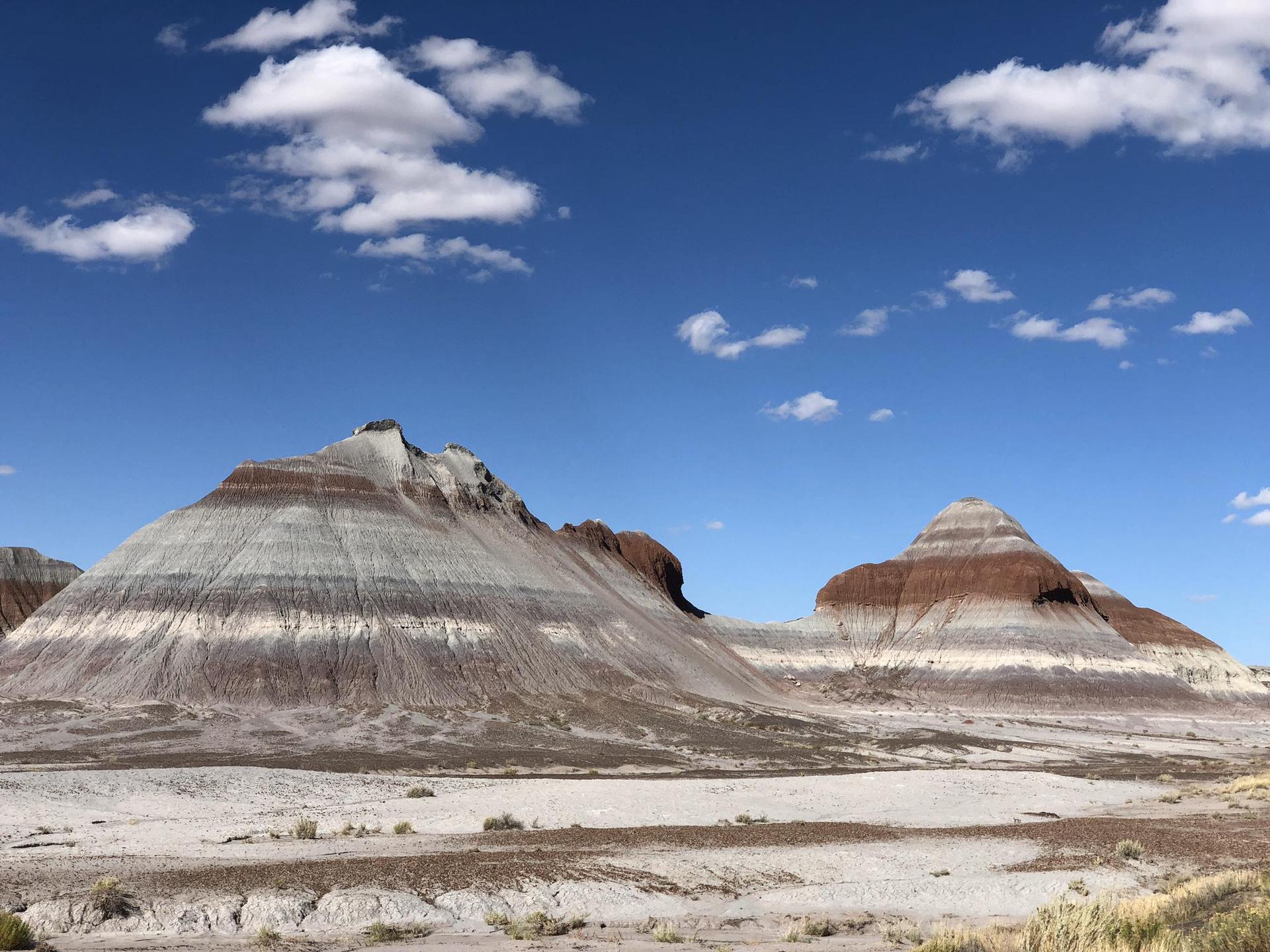 Two prominent striped hills in a wide desert under a bright blue sky.