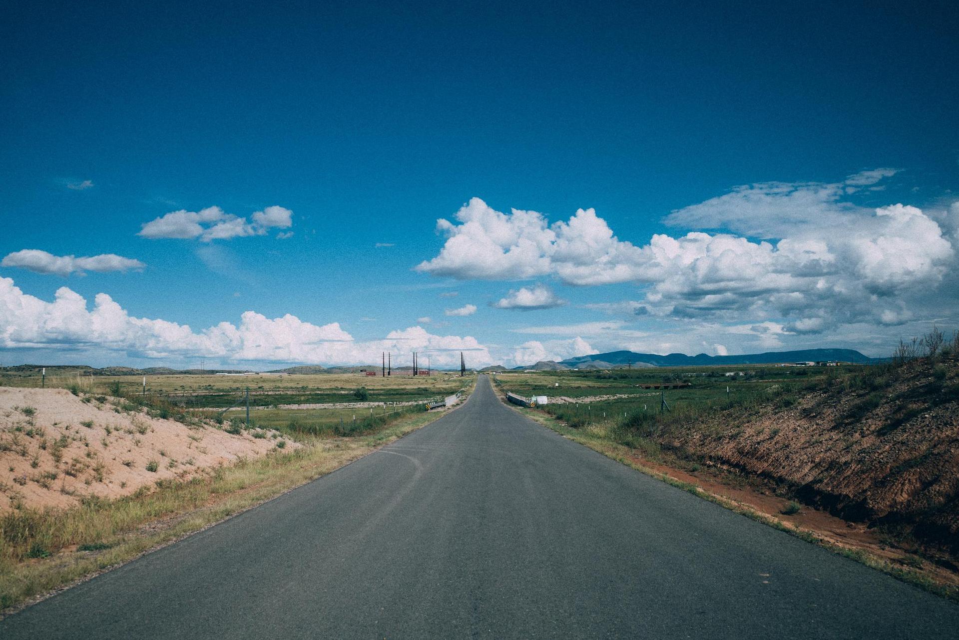 Empty road stretching into the distance under a bright blue sky with clouds.
