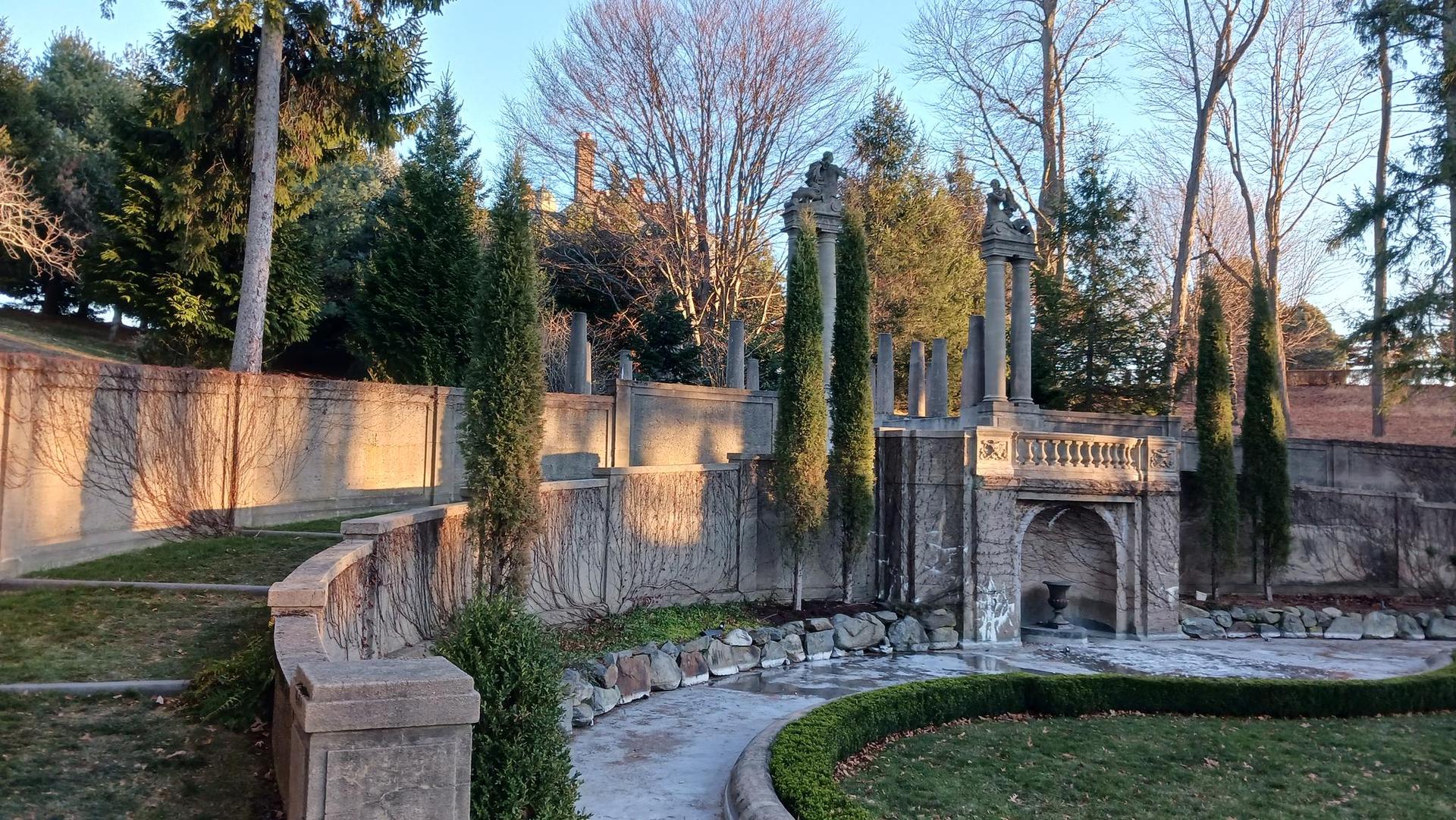 Stone wall with cypress trees bathed in warm, late afternoon light.