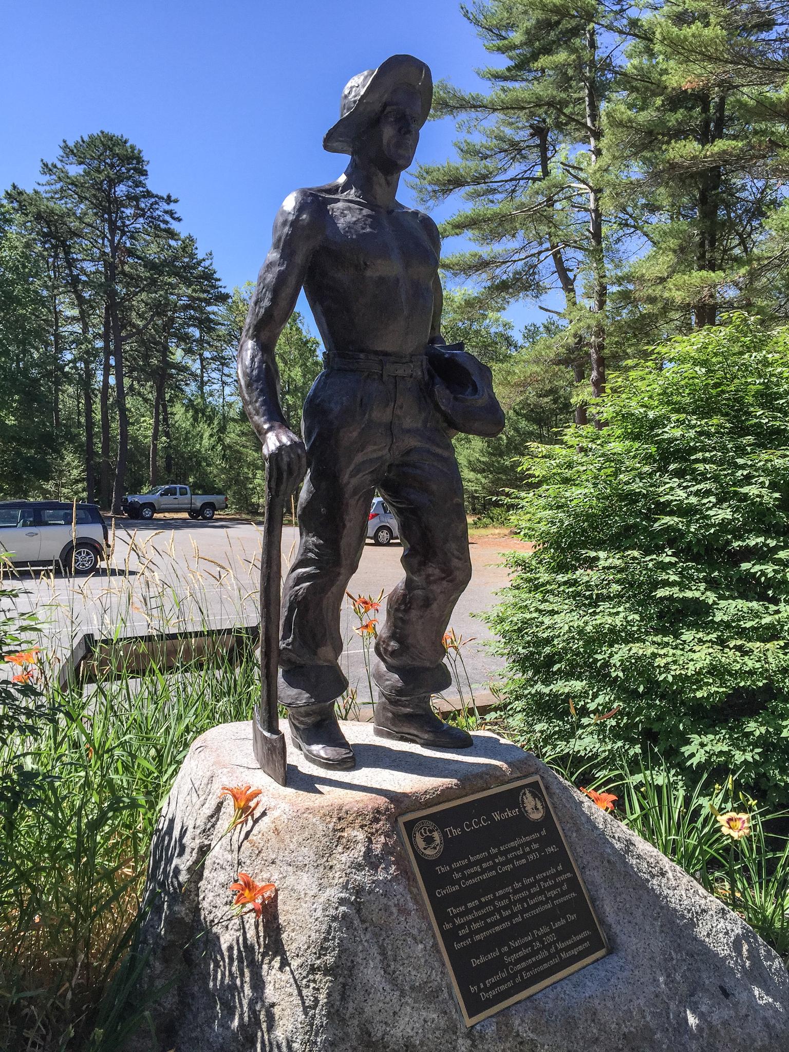 Bronze statue of a man with a tool on a rock, sunny day.