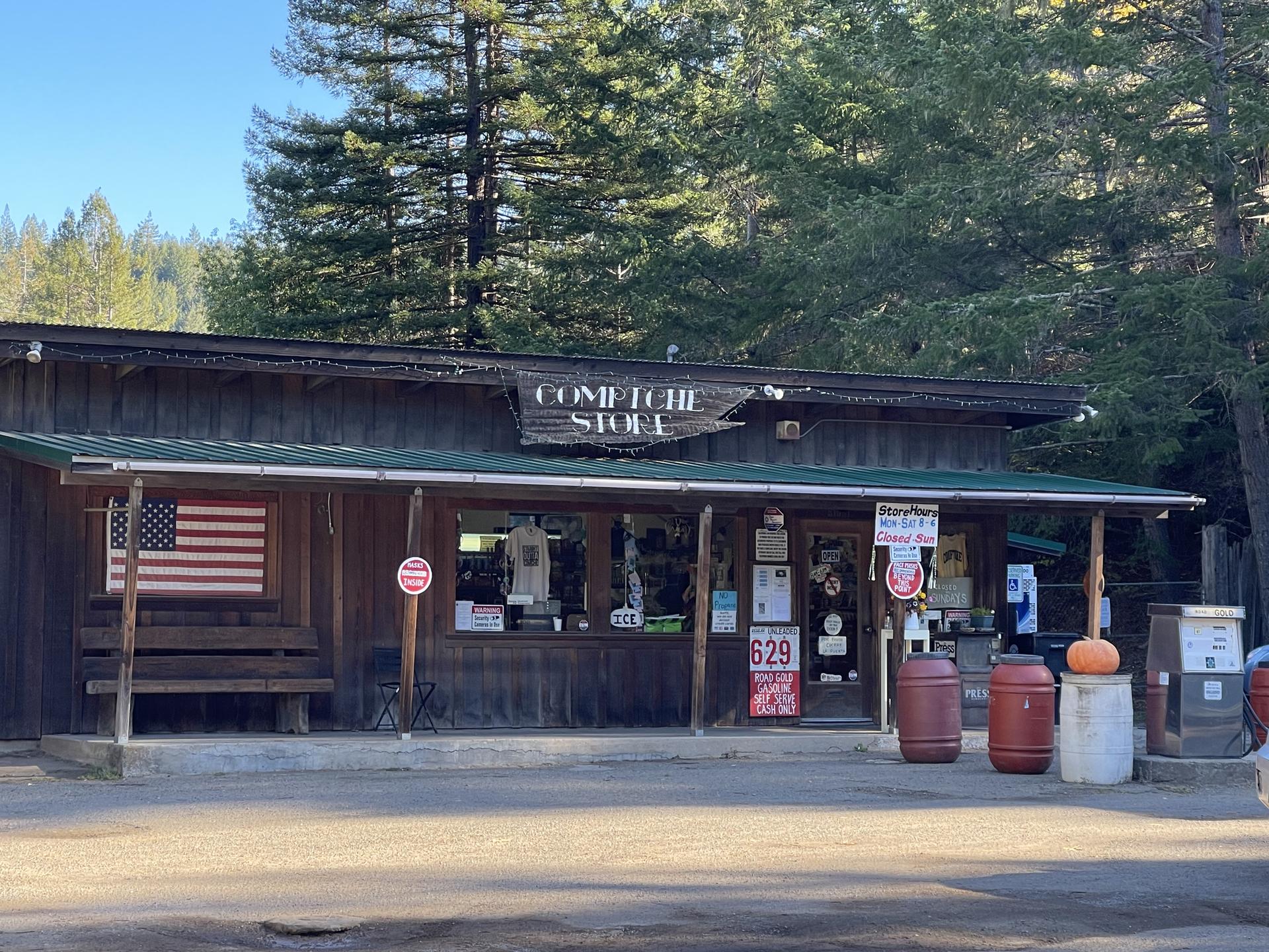 Rustic wooden store with a porch and American flag, backed by a forest.