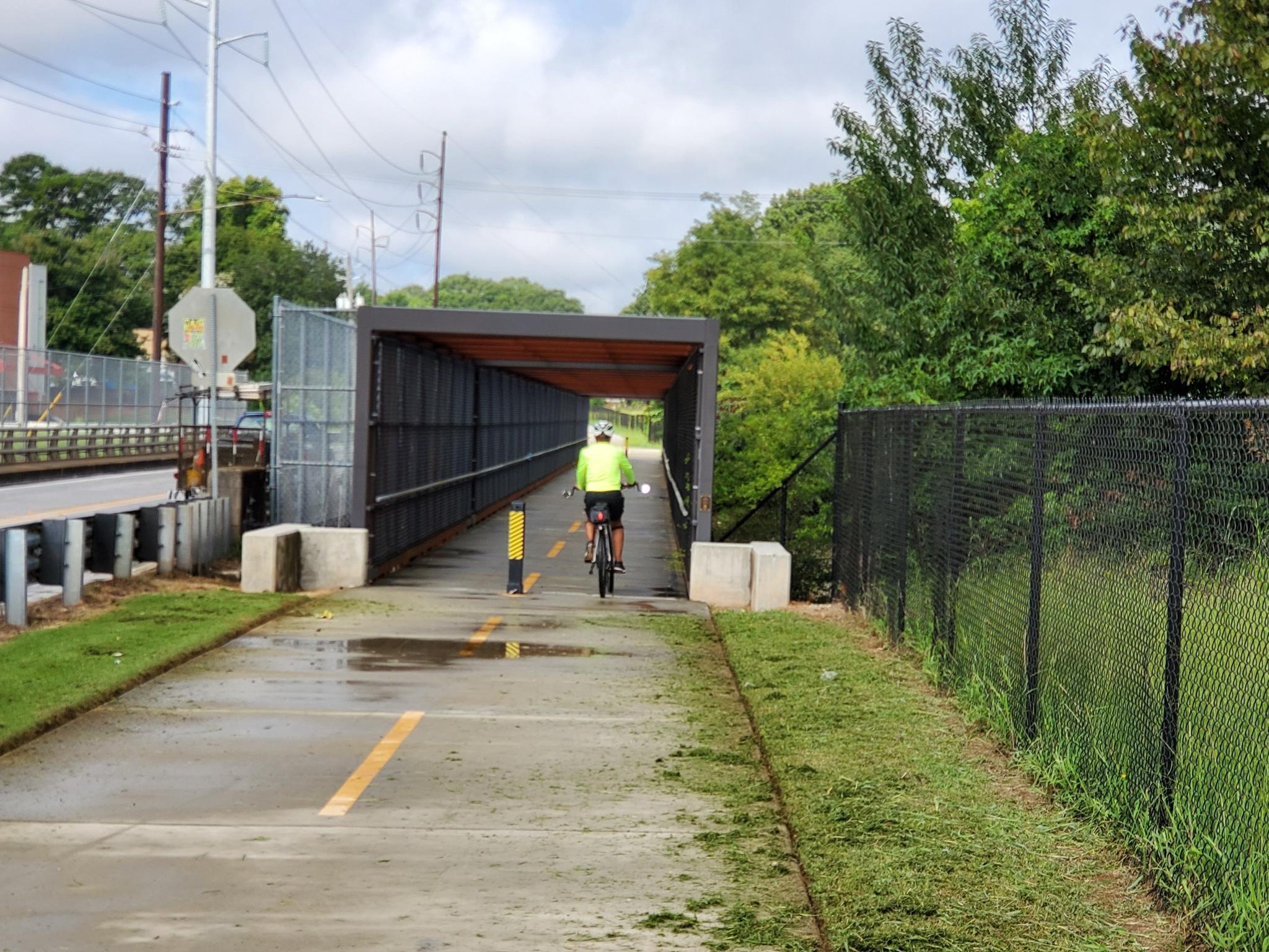 Cyclist in yellow vest rides into a covered bridge on a paved path.