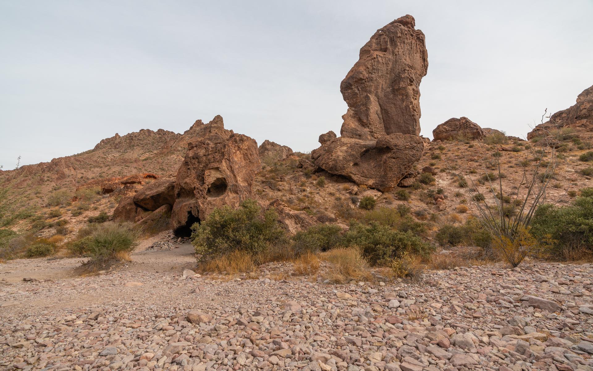 Large rock formations and a cave entrance in a rocky desert landscape.