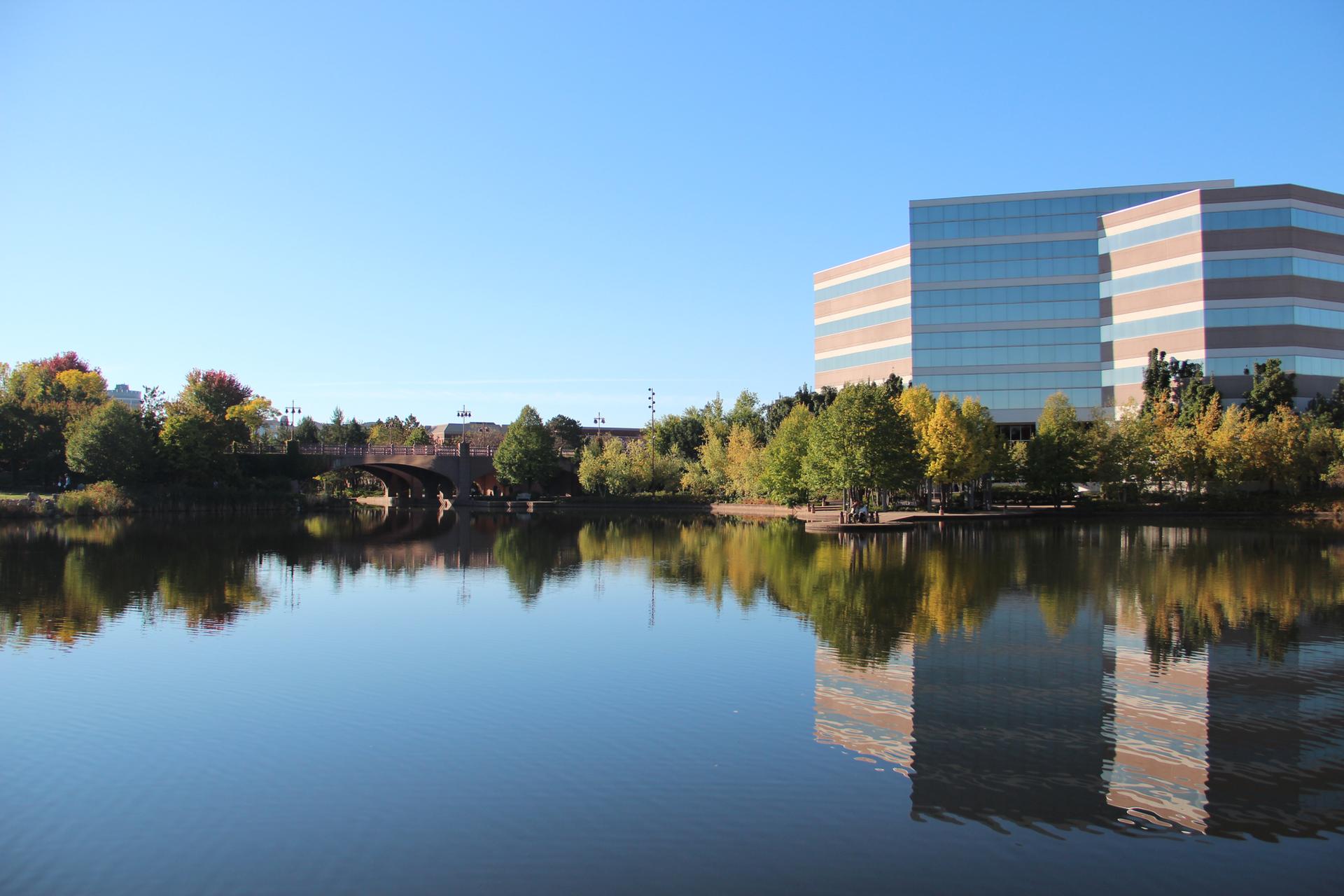 A modern building and autumn trees reflect on a calm lake.