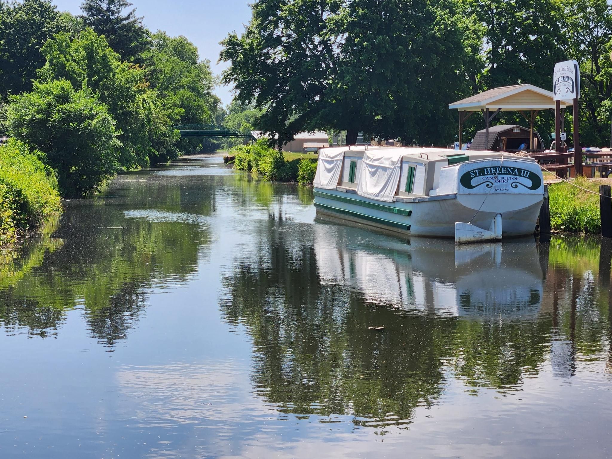 A white and green boat docked on a calm, tree-lined canal. - St Helena Heritage Park – Cherry Street Creamery loop from Canal Fulton