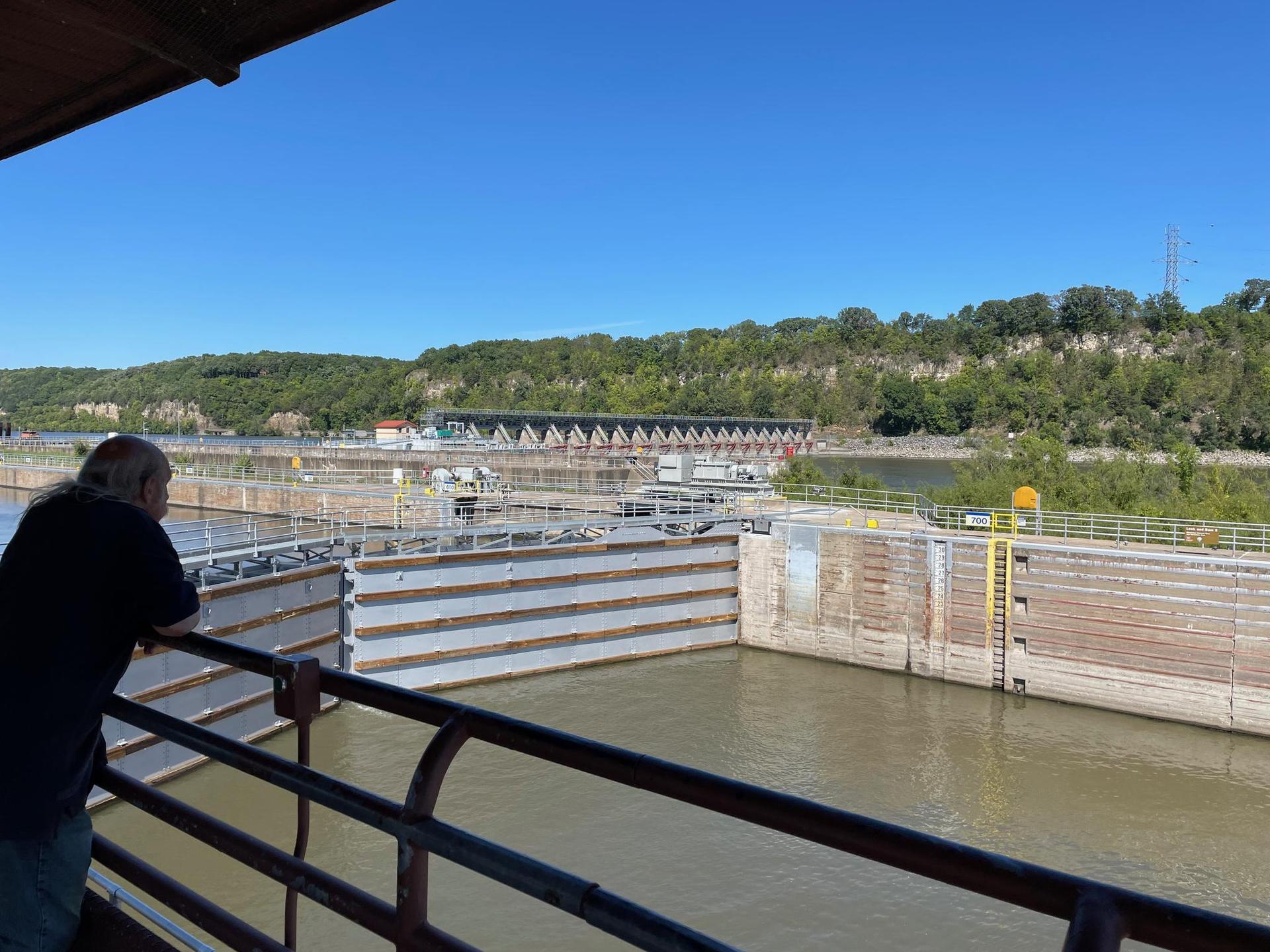 Man views a large river lock system under a clear blue sky.