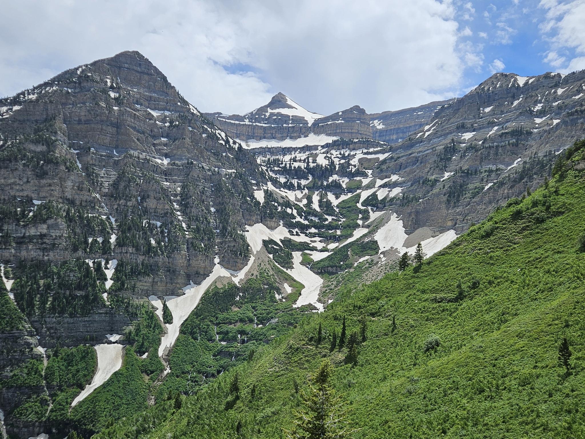 Majestic mountains with snow patches and green slopes under a cloudy sky.